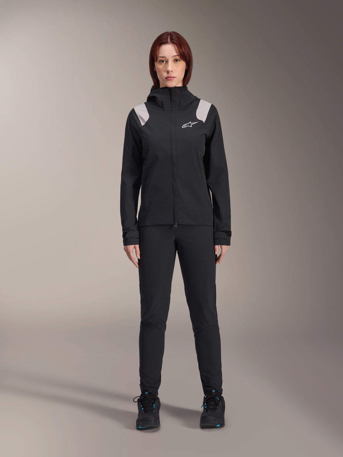 Alpinestars Stella A-Dura regnjakke, MTB-regnjakke til damer, sort med lysegrå skulderdetaljer og hvidt logo, bæres med matchende sorte bukser og sko, med hætte og justerbare manchetter, designet til mountainbike-trail kørsel