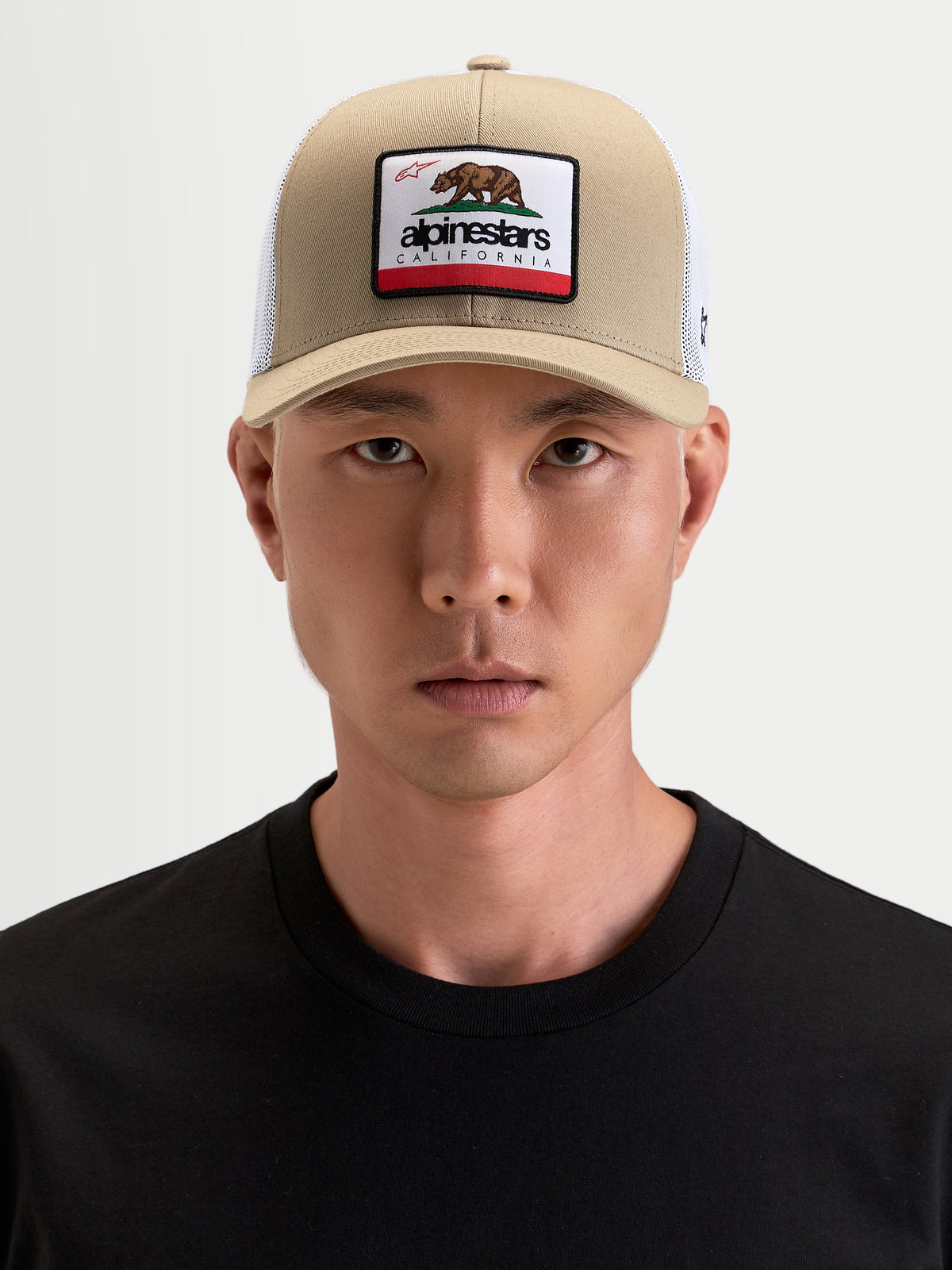 Alpinestars Cali 2.0 kasket, sportswear trucker cap i khaki og hvid, med buet skygge, struktureret twillkrone og California bear-frontpatch, båret af mandlig model