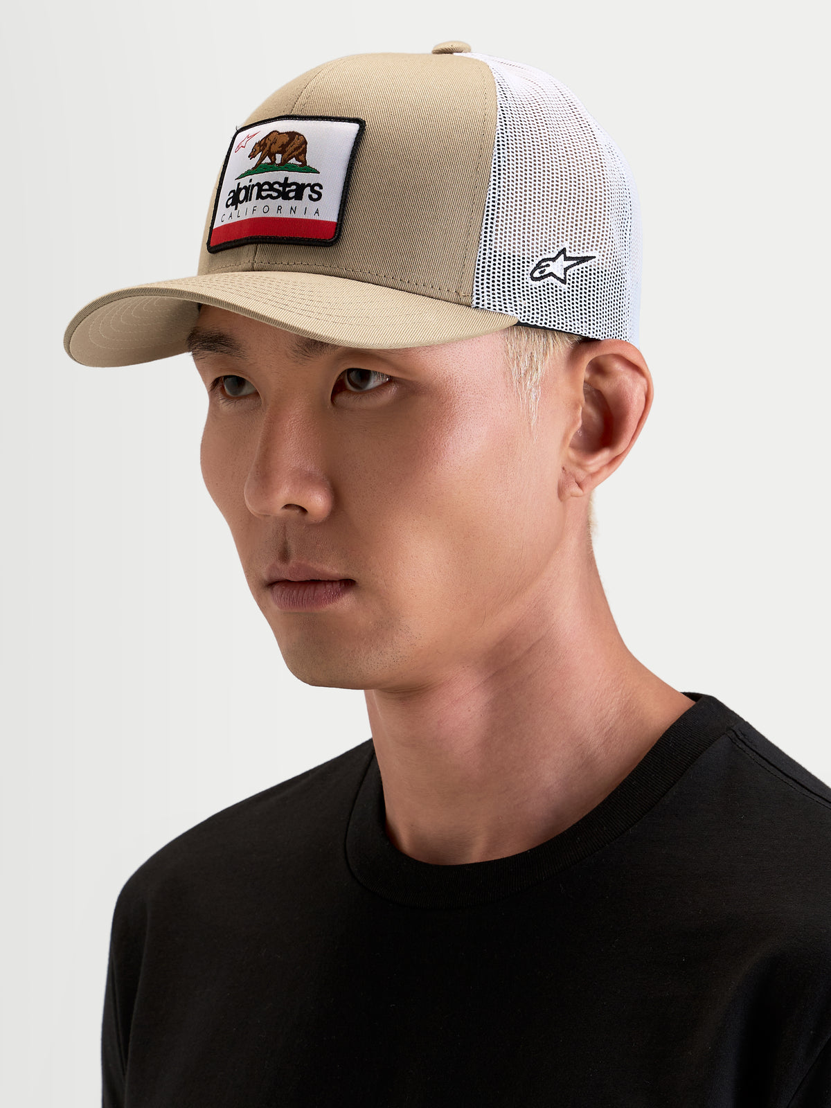 Alpinestars Cali 2.0 kasket, sportswear trucker cap i khaki og hvid, båret af model, med buet skygge, struktureret twill-krone og vævet California-mærke på fronten