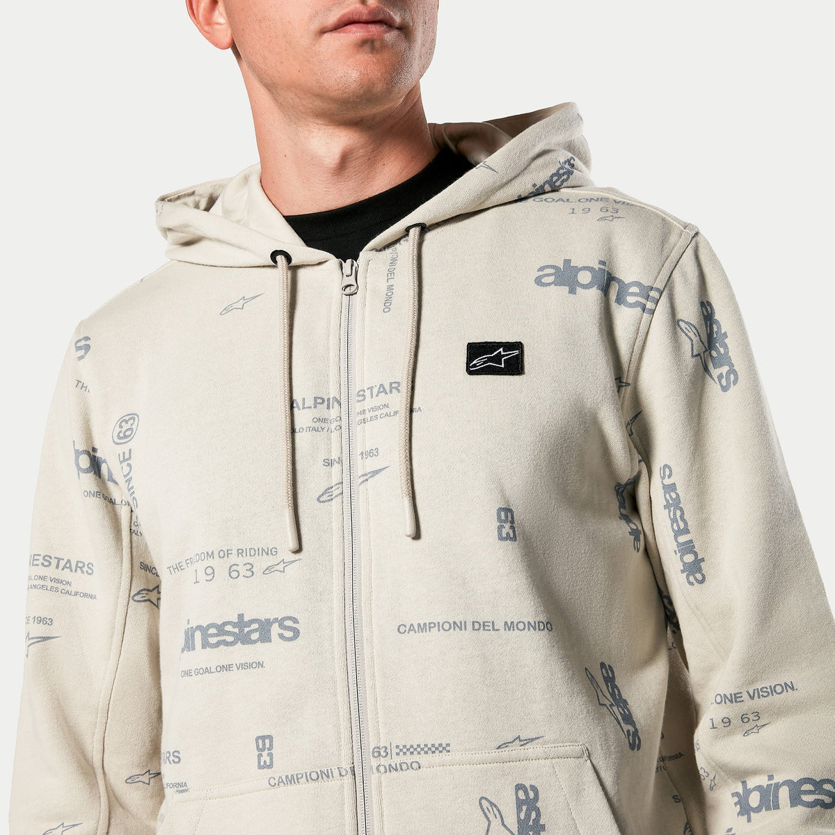 Alpinestars Plenitude hættetrøje, fleece med lynlås i Off White, all-over grafisk print med 'alpinestars' og '1963' tekst, sort broderet logopatch på brystet, hætte med snoretræk, afslappet motorsport-inspireret streetwear