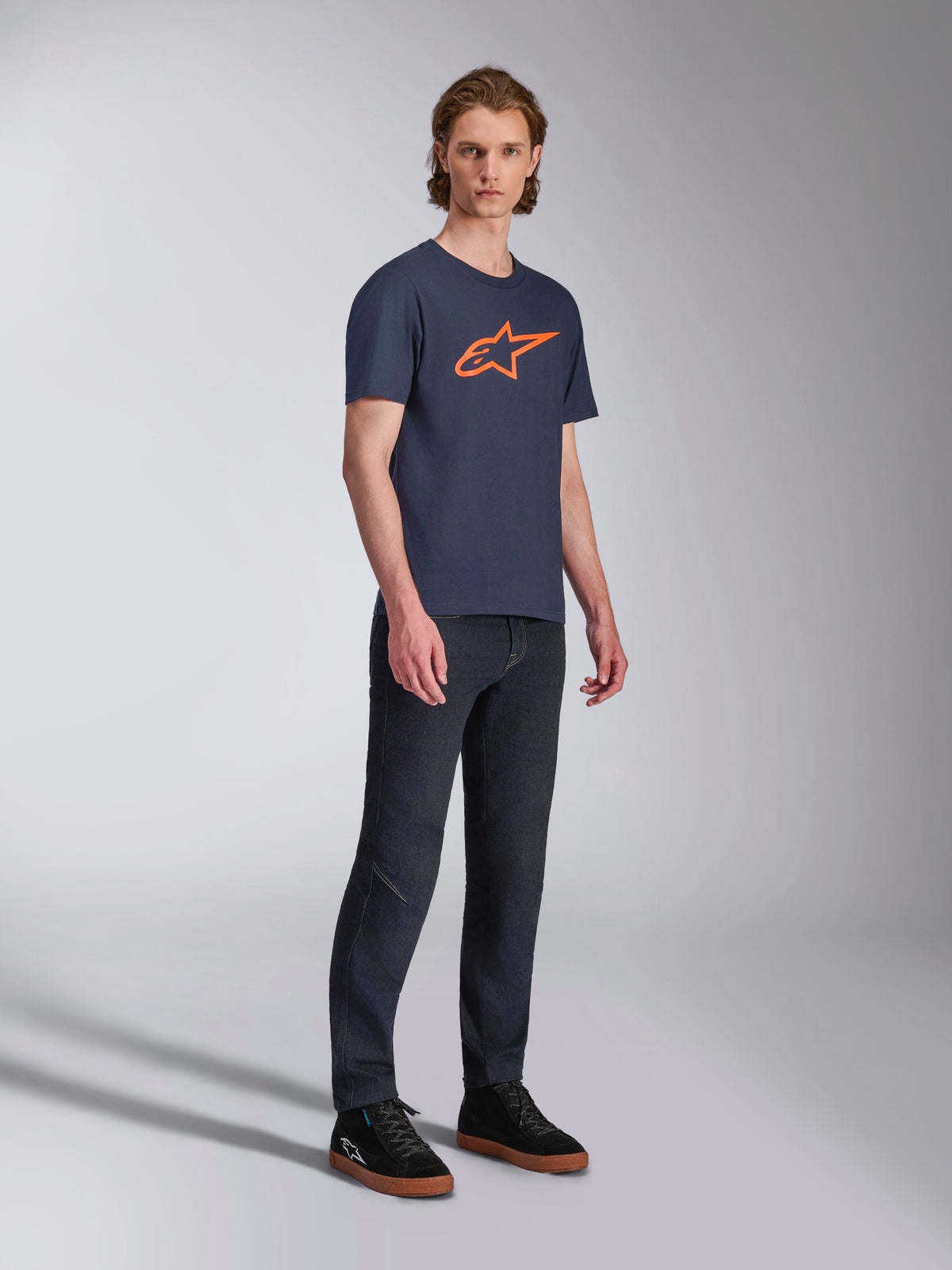 Alpinestars Ageless 2.0 CSF Tee, kortærmet t-shirt, mørkeblå med orange stjernelogo, båret med mørke denimjeans og sorte sneakers, afslappet motorsport-inspireret streetwear