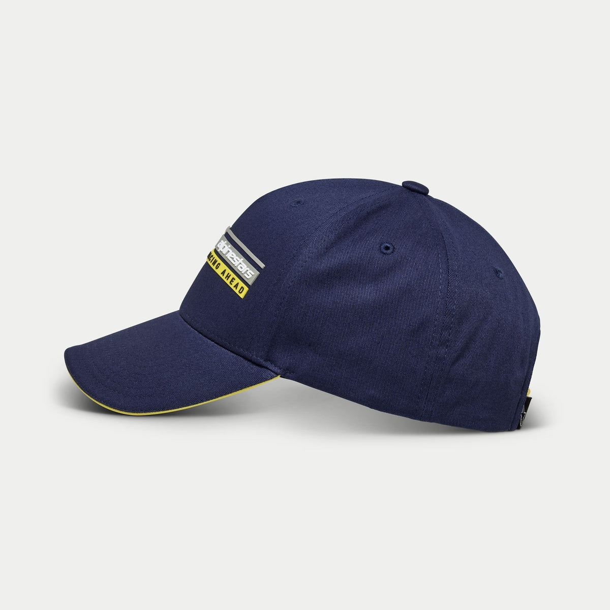 Alpinestars Par Hat, navyblå baseballkasket, set fra siden, struktureret krone med kurvet skygge og gul sandwich-detalje, Alpinestars Racing Ahead lineært logo 3D-broderi, casual motorsports-inspireret hovedbeklædning