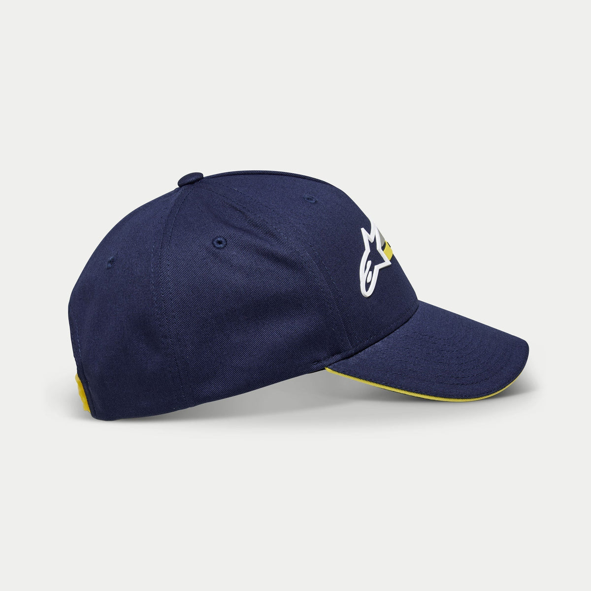 Alpinestars Par Hat, marineblå baseball cap, set fra siden med hvidt og gult broderet logo, kurvet skygge med gul sandwich-kant, afslappet struktureret hovedbeklædning
