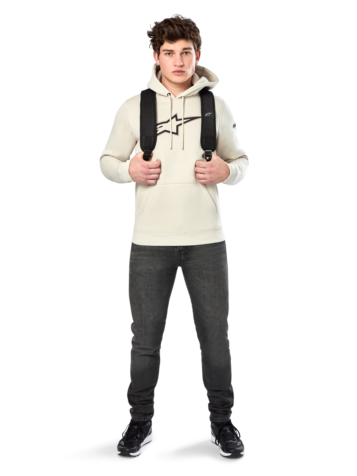 Alpinestars Insignia Hoodie, casual streetwear, Off White fleece pullover, carbon fiber look logo with red outline, drawstring hood, kangaroo pocket, worn by model with black backpack and dark grey jeans