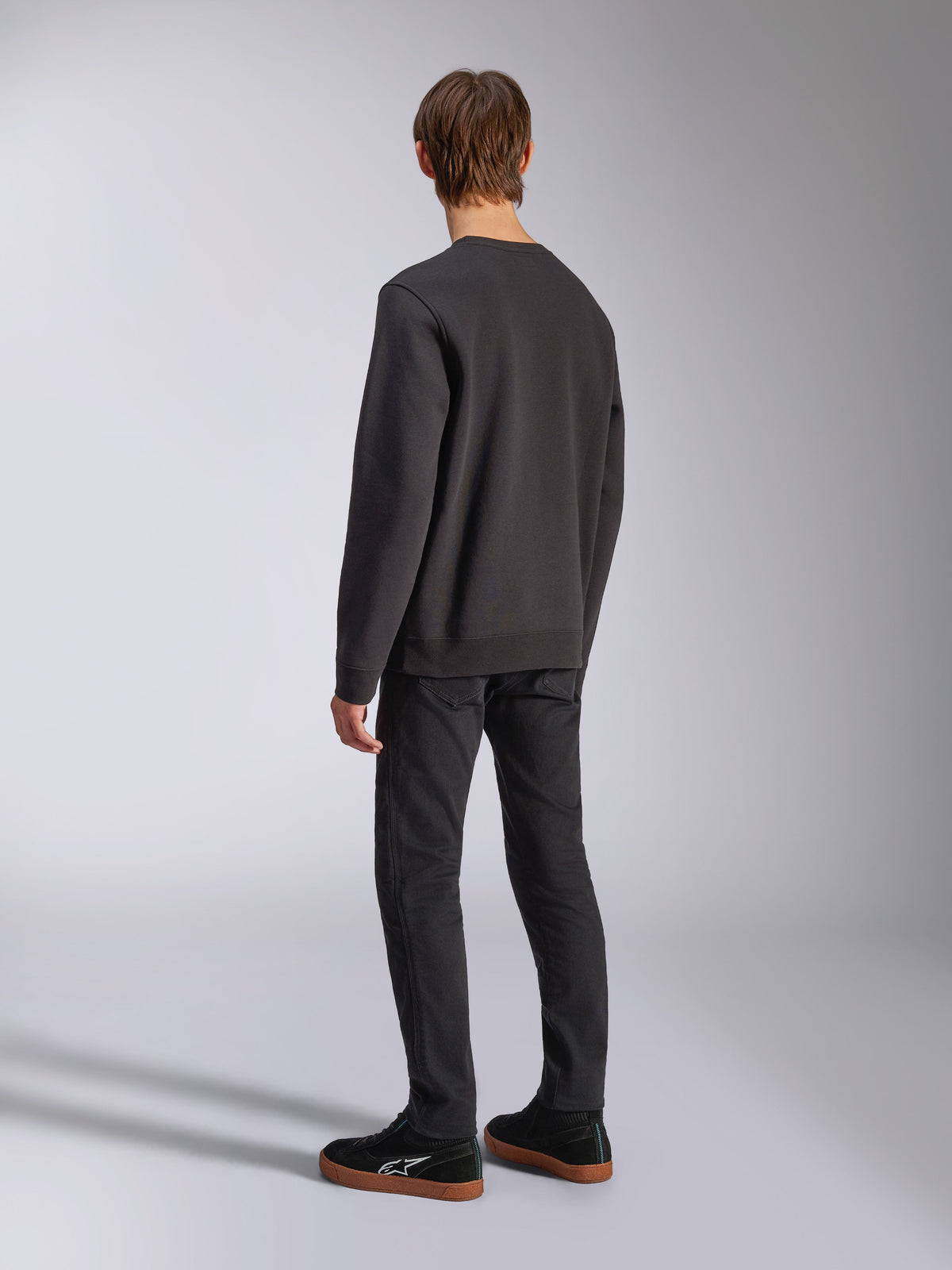 Alpinestars Positive Crew, sort pullover sweatshirt, set bagfra på model, afslappet motorsport-inspireret streetwear, med ribkant forneden og ved manchetterne.