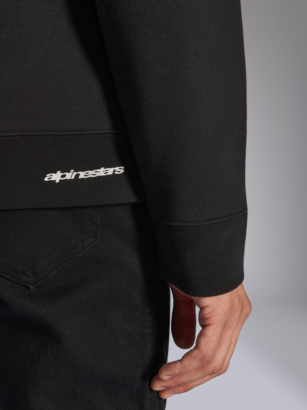 Alpinestars Positive Crew, sort pullover sweatshirt, tæt detalje af ribkant og ærmemanchet med hvidt Alpinestars-logo, premium materialetekstur, afslappet motorsportsinspireret sportstøj