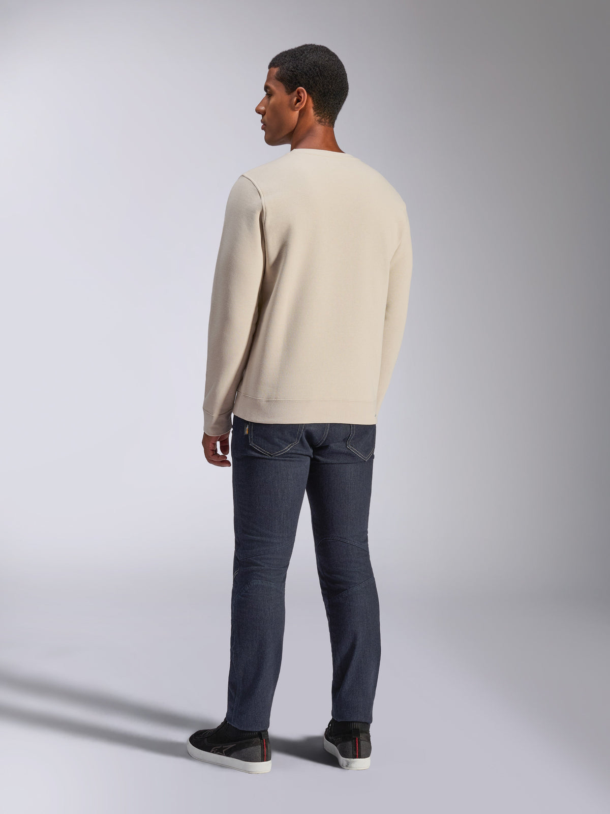 Alpinestars Positive Crew, Off White crewneck sweatshirt, set bagfra på model, kombineret med mørke denimjeans og sorte sneakers, afslappet motorsport-streetwear, med ribstrikkede manchetter og kant