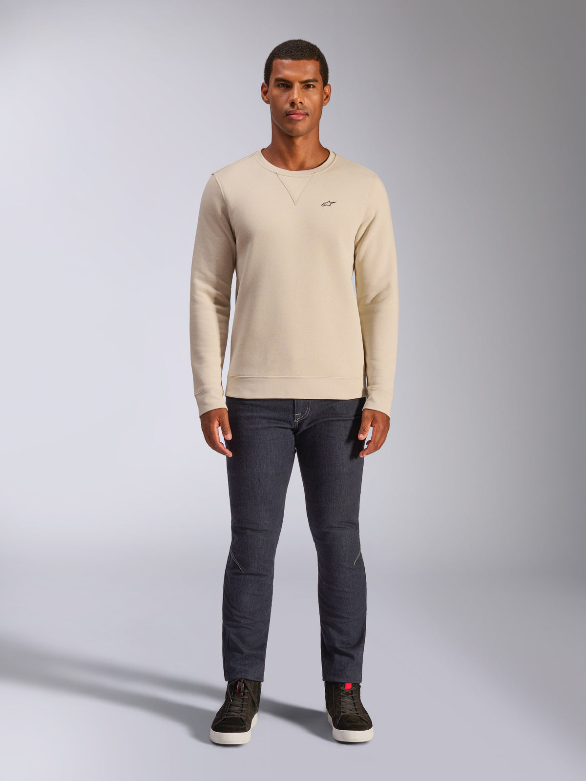 Alpinestars Positive Crew, off-white sweatshirt med rund hals, lille sort logo på brystet, ribkant ved manchetter og søm, trekantede syninger ved halsen, afslappet motorsport-streetwear båret med mørke jeans