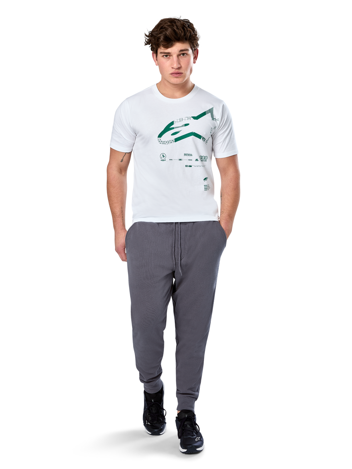 Alpinestars Geografica CSF Tee, kortærmet t-shirt, hvid, grønt Astars-logo med geografisk multi-tech-grafik, båret med grå joggingbukser og sorte sneakers, afslappet motorsport-streetwear