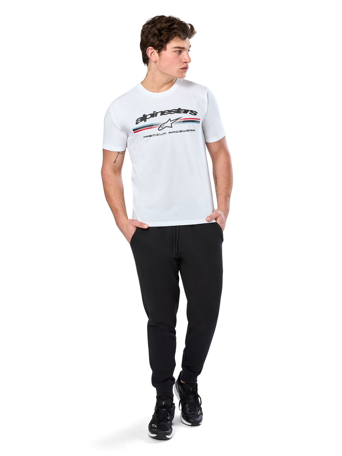 Alpinestars Prevail CSF Tee, kortærmet T-shirt, hvid, med trefarvet stribelogo i paddock-stil og Alpinestars-branding på fronten, båret af en model med sorte joggingbukser og sorte sneakers, afslappet motorsport streetwear