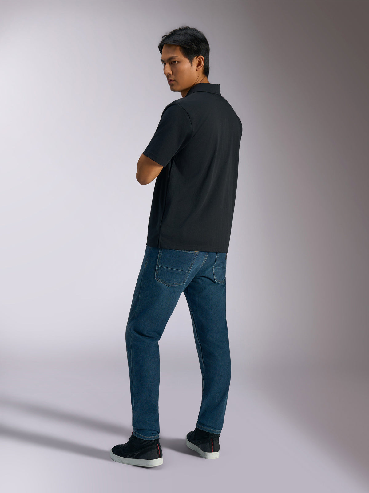 Alpinestars Impetus Sport Polo, sort, kortærmet polo shirt med mock mesh-tekstur og stolpelukning med tre knapper, båret af en model med blå jeans og sorte sneakers, afslappet motorsport-inspireret streetwear