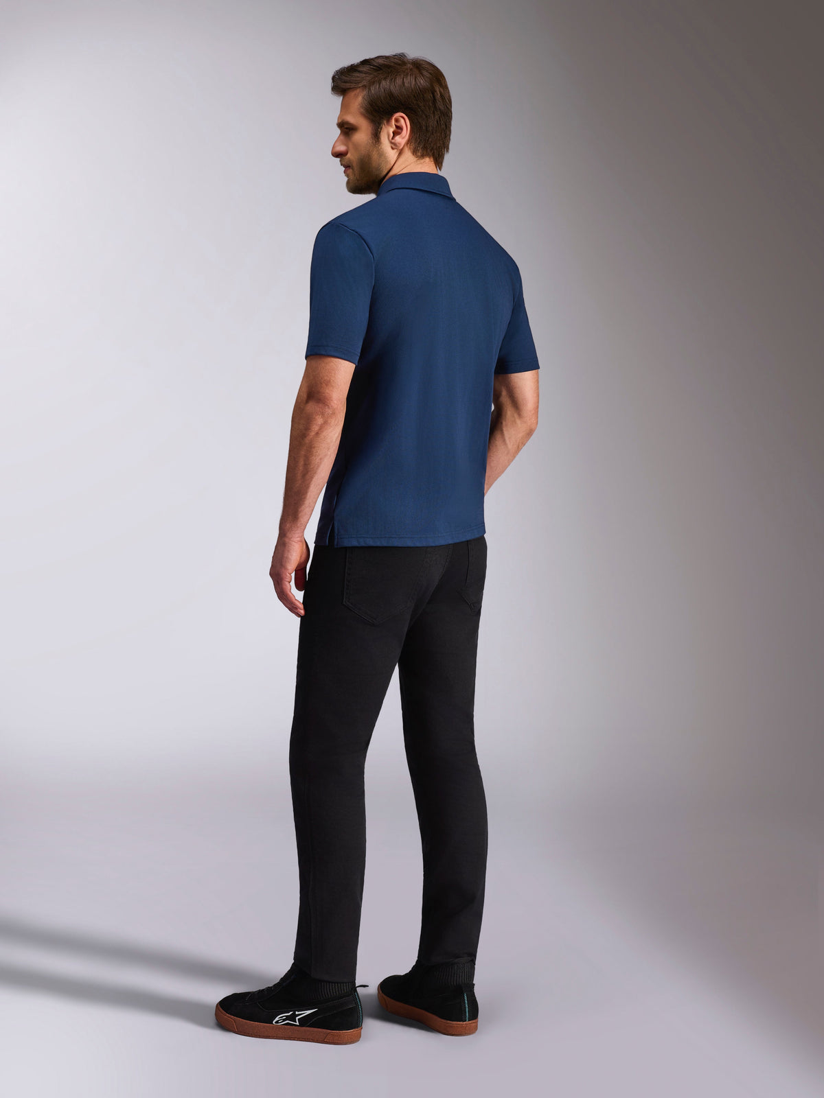 Alpinestars Impetus Sport Polo, mørkeblå kortærmet poloshirt, set bagfra og fra siden på model, kombineret med sorte bukser og sorte sneakers, afslappet motorsport lifestyle sportstøj