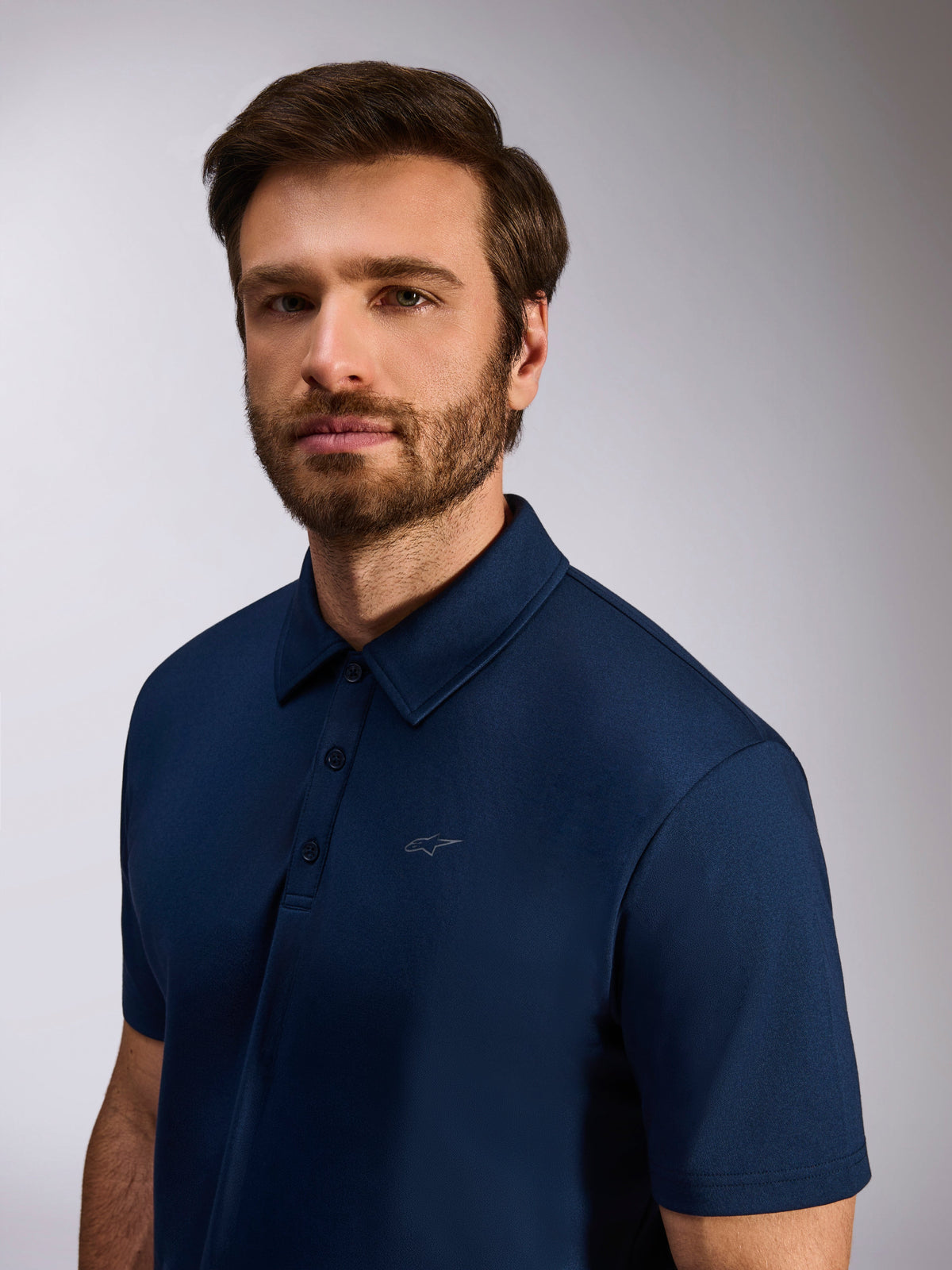Model iført Alpinestars Impetus Sport Polo, marineblå, kortærmet polo i mock mesh, med stolpelukning med tre knapper og diskret Astars-logo på brystet, afslappet lifestyle-beklædning til motorsport