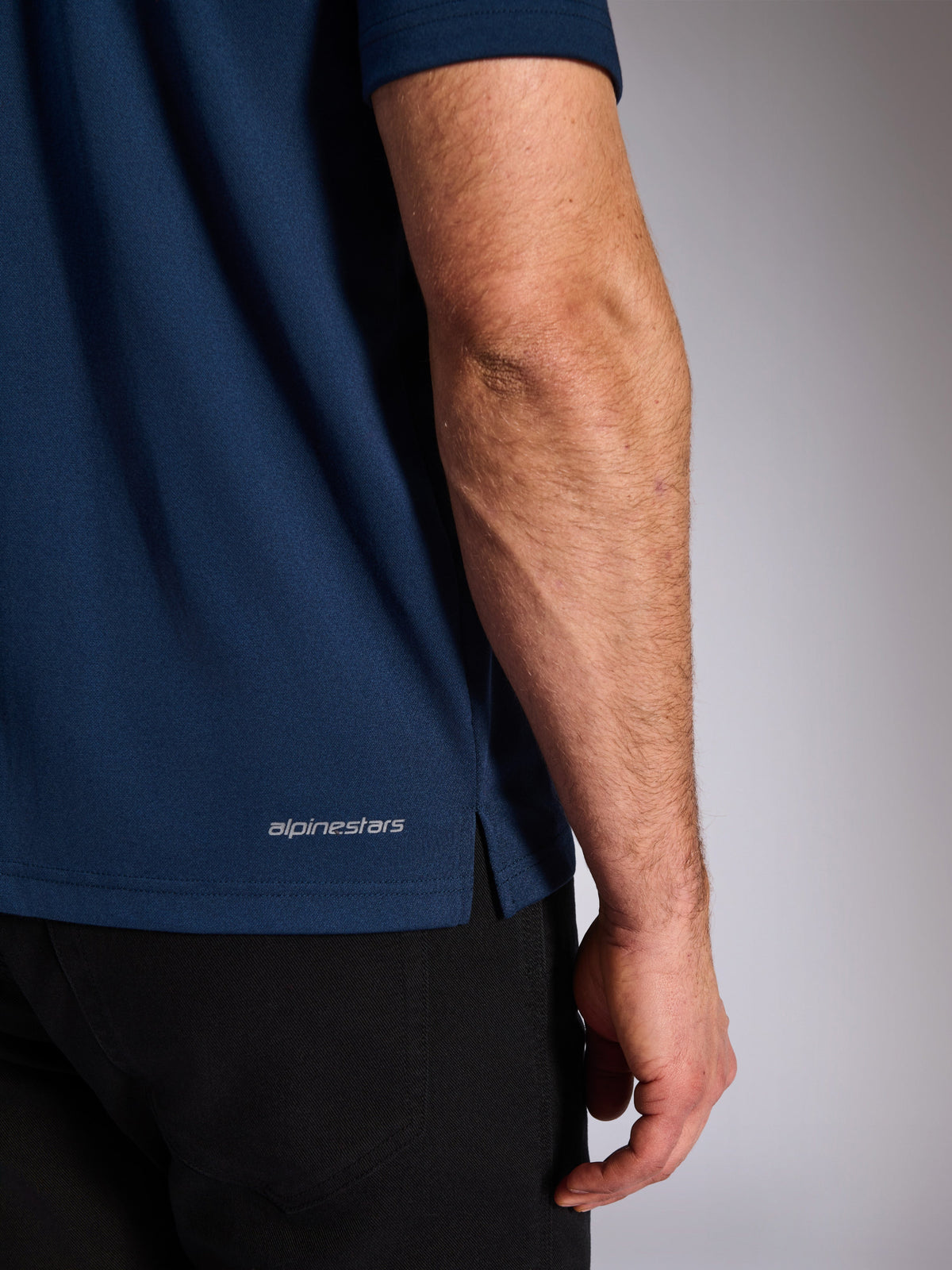 Alpinestars Impetus Sport Polo, Navy, nærbillede af den nederste kant, der viser Alpinestars-ordmærket og sideslids, mock-mesh-striktekstur, afslappet motorsportstøj