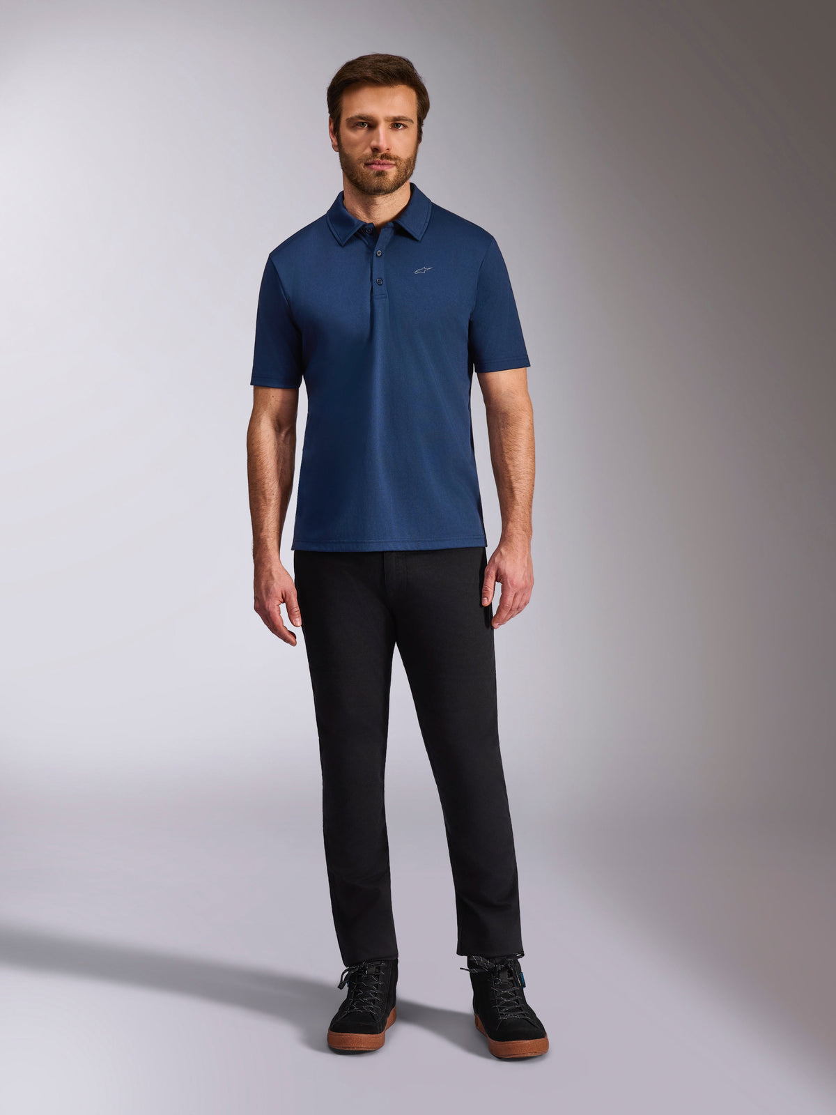Alpinestars Impetus Sport Polo, kortærmet poloshirt, navyblå, lille sølvfarvet Astars-logo på brystet, stolpelukning med tre knapper, bæres af model med sorte bukser og støvler, afslappet motorsport-inspireret sportstøj