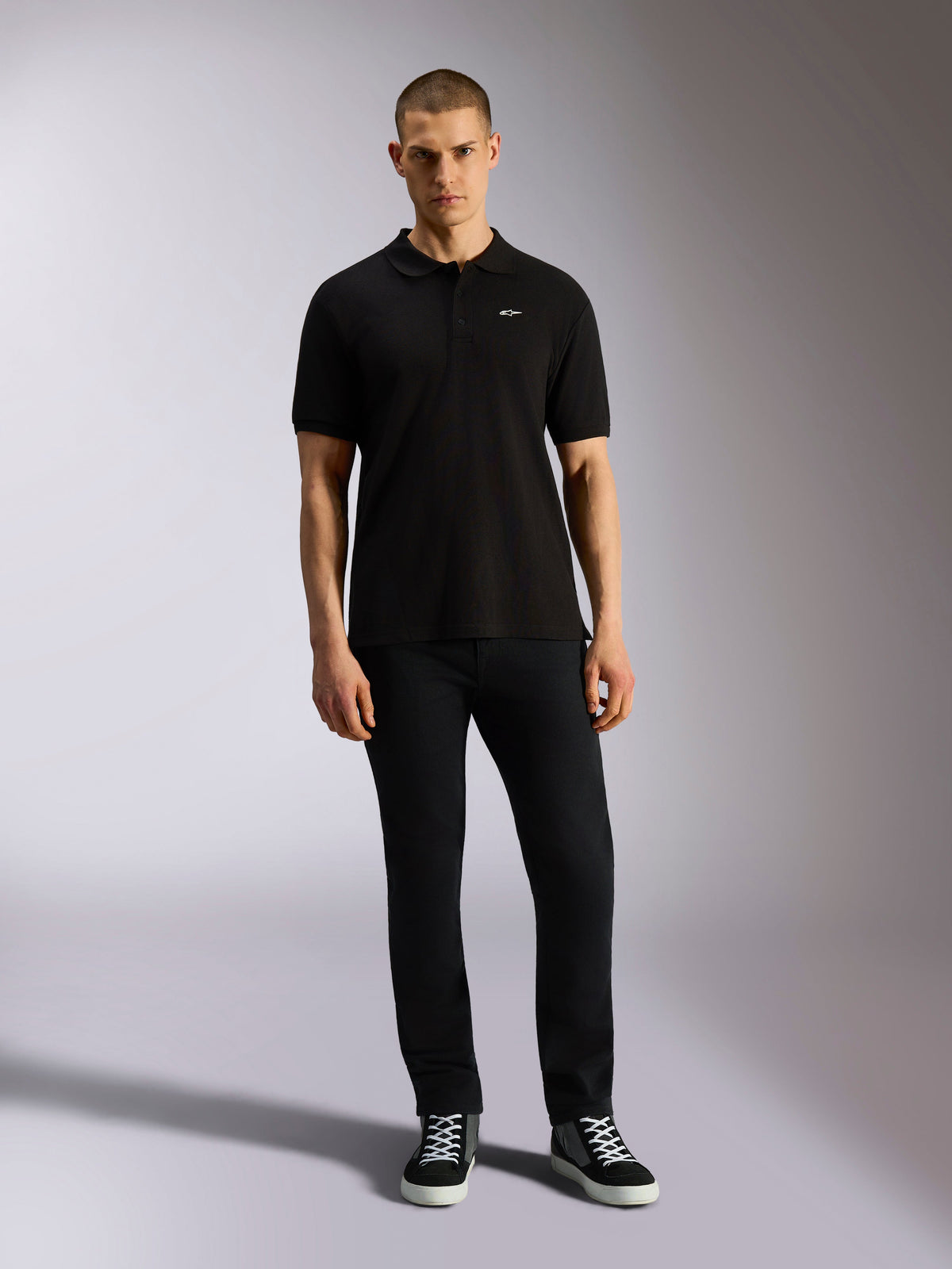 Alpinestars Endeavor Classic Polo, kortærmet piqué-poloshirt, sort, lille hvidt Astars-logo på brystet, ribkrave og ribkanter på ærmerne, bæres af model med sorte bukser og sneakers, afslappet motorsport-streetwear