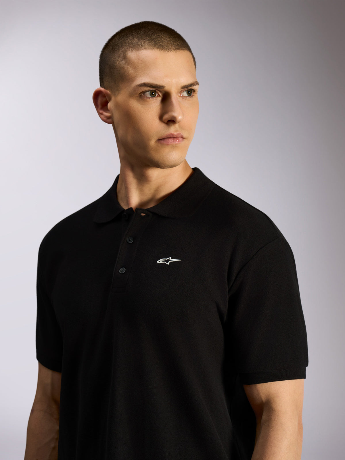 Alpinestars Endeavor Classic Polo, sort piqué polo båret af en mandlig model, lille hvidt Astars-logo på brystet, tre-knaps stolpelukning og ribkrave, afslappet motorsport-streetwear