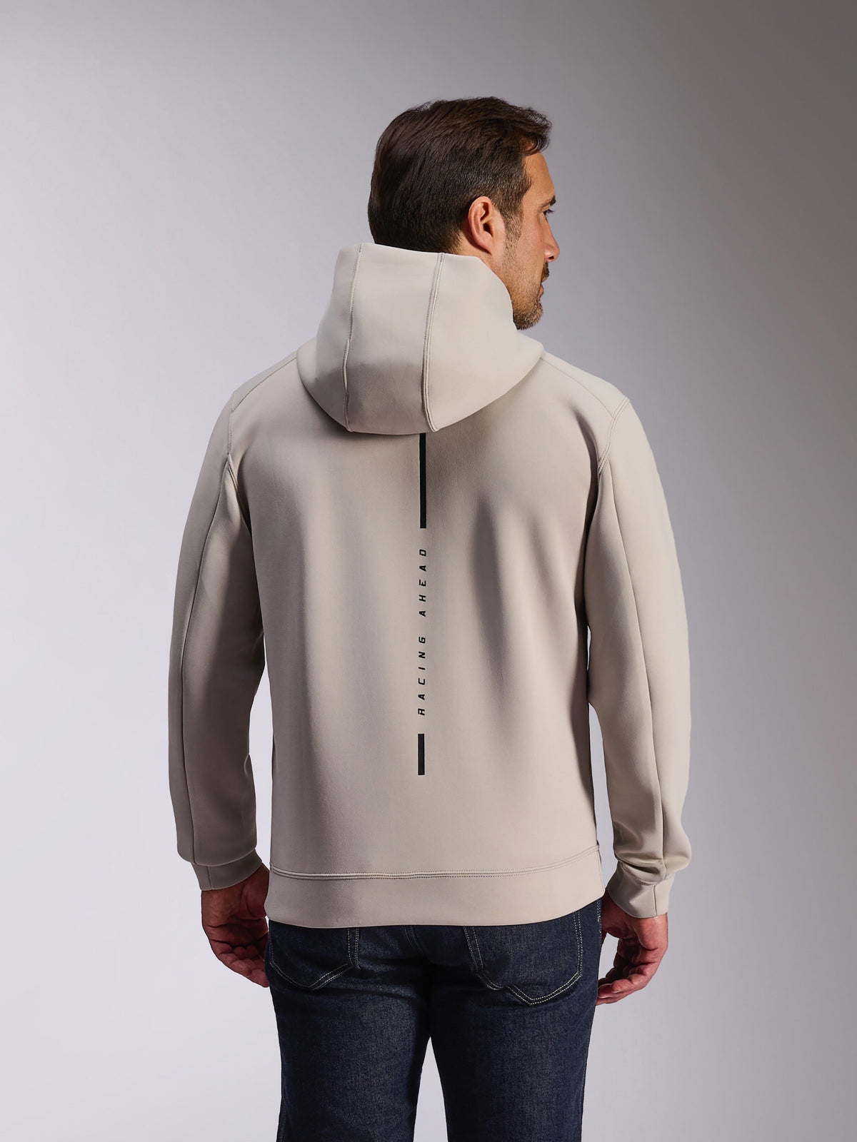 Alpinestars Insight hættetrøje i Cement, set bagfra på model iført en lysegrå pullover-sweatshirt, med et sort lodret stribelogo med teksten 'RACING AHEAD', afslappet motorsport-inspireret hættetrøje i dobbelt-face fleece.