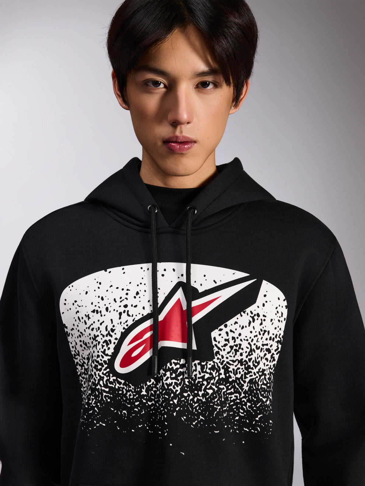 Alpinestars Obsessed hættetrøje, sort pullover i fleece, med et rødt og hvidt Astars-logo inde i en hvid prikket MX-graduering på brystet, båret af en model, afslappet motorsport-streetwear med justerbar hætte med snoretræk