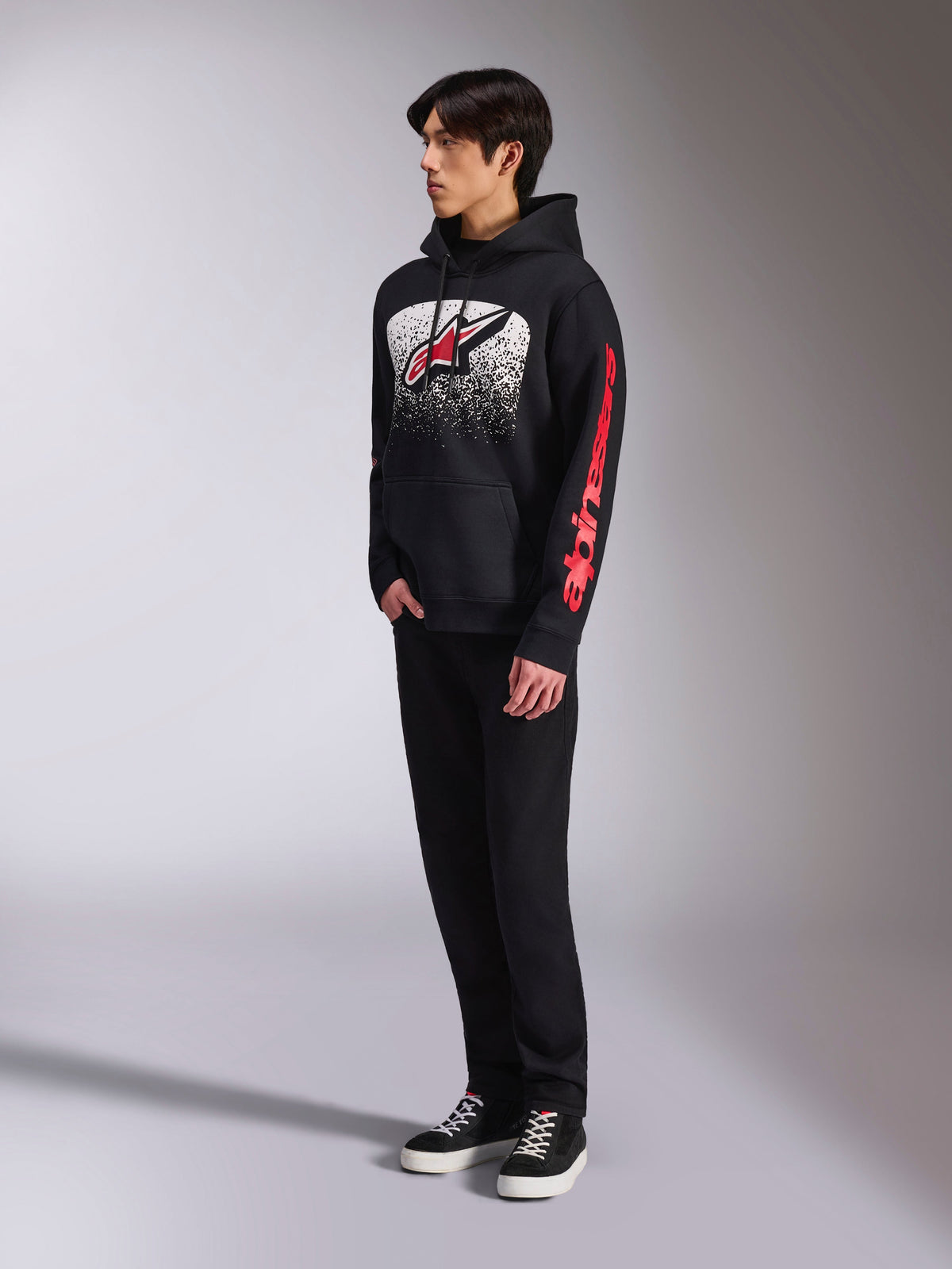 Alpinestars Obsessed hættetrøje, sort pullover-fleece, med en stor hvid plettet grafik på brystet, et rødt Astars-logo og rød branding på ærmerne, båret af en model med sorte bukser og sneakers, afslappet motorsport-streetwear
