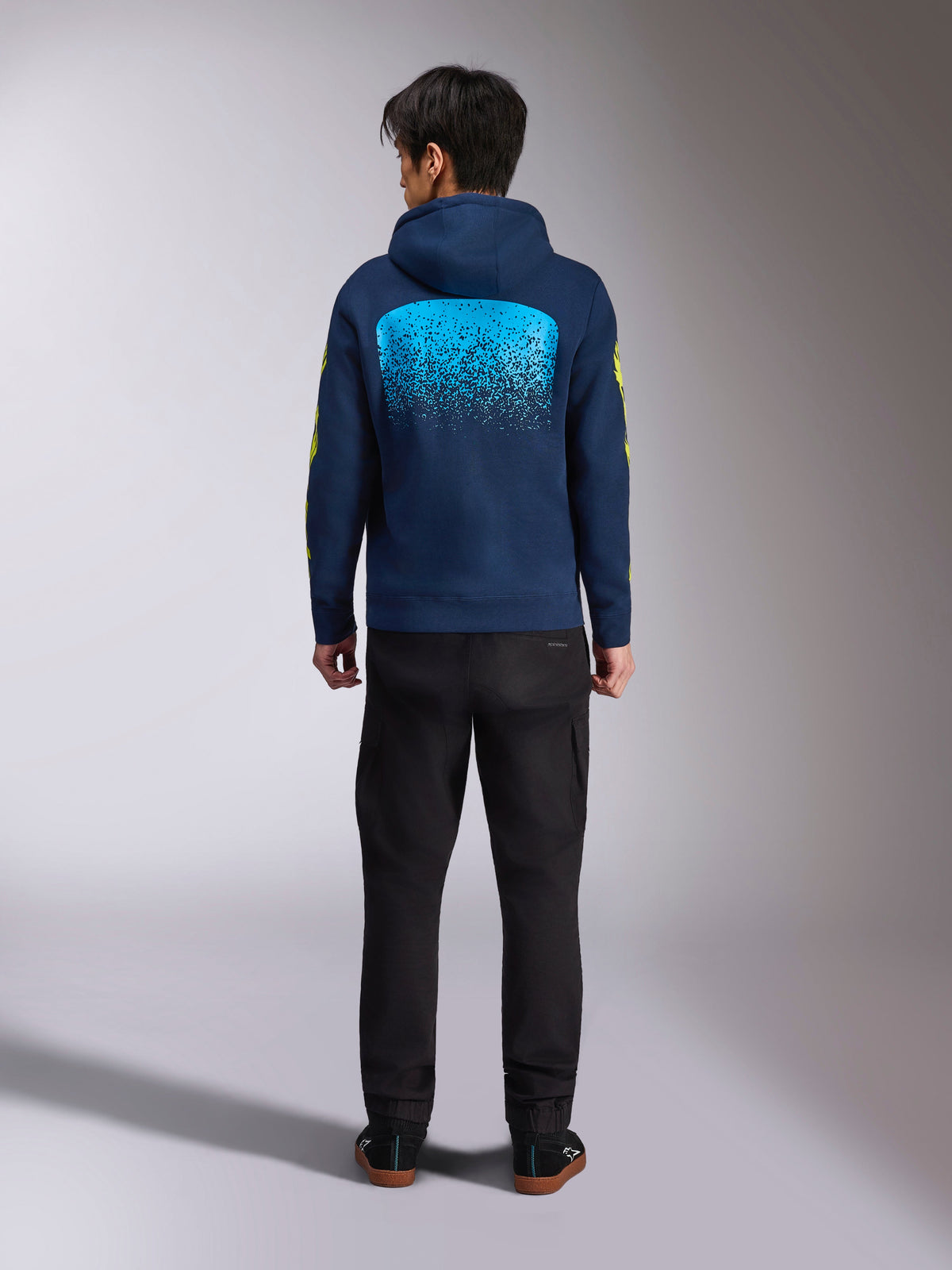 Alpinestars Obsessed hættetrøje i mørkeblå, set bagfra med stor cyanblå MX-gradueringsgrafik og gule logoer på ærmerne, afslappet motorsport-inspireret pullover-fleece.