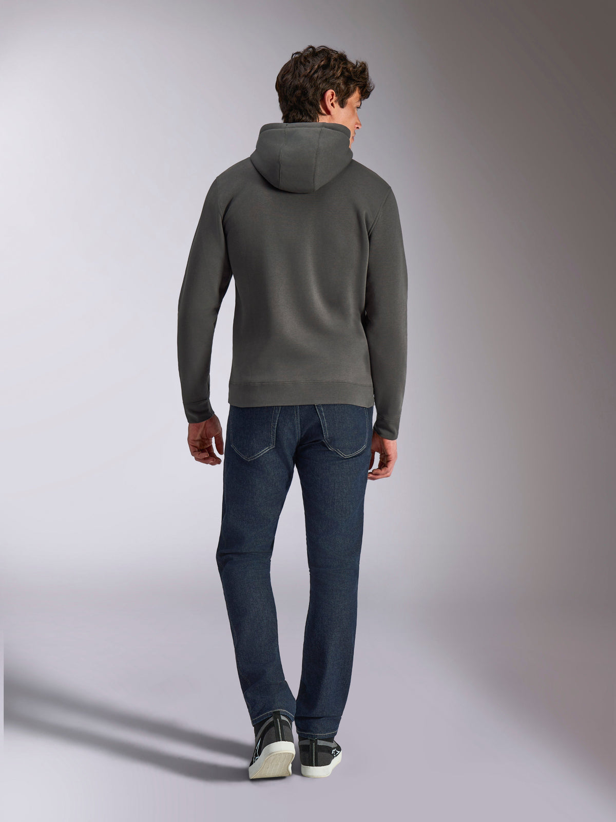 Alpinestars Ellipsoid hættetrøje, gunmetal grå pullover-hættetrøje, set bagfra, båret af model med mørke denimjeans og sorte sneakers, afslappet motorsport-inspireret streetwear