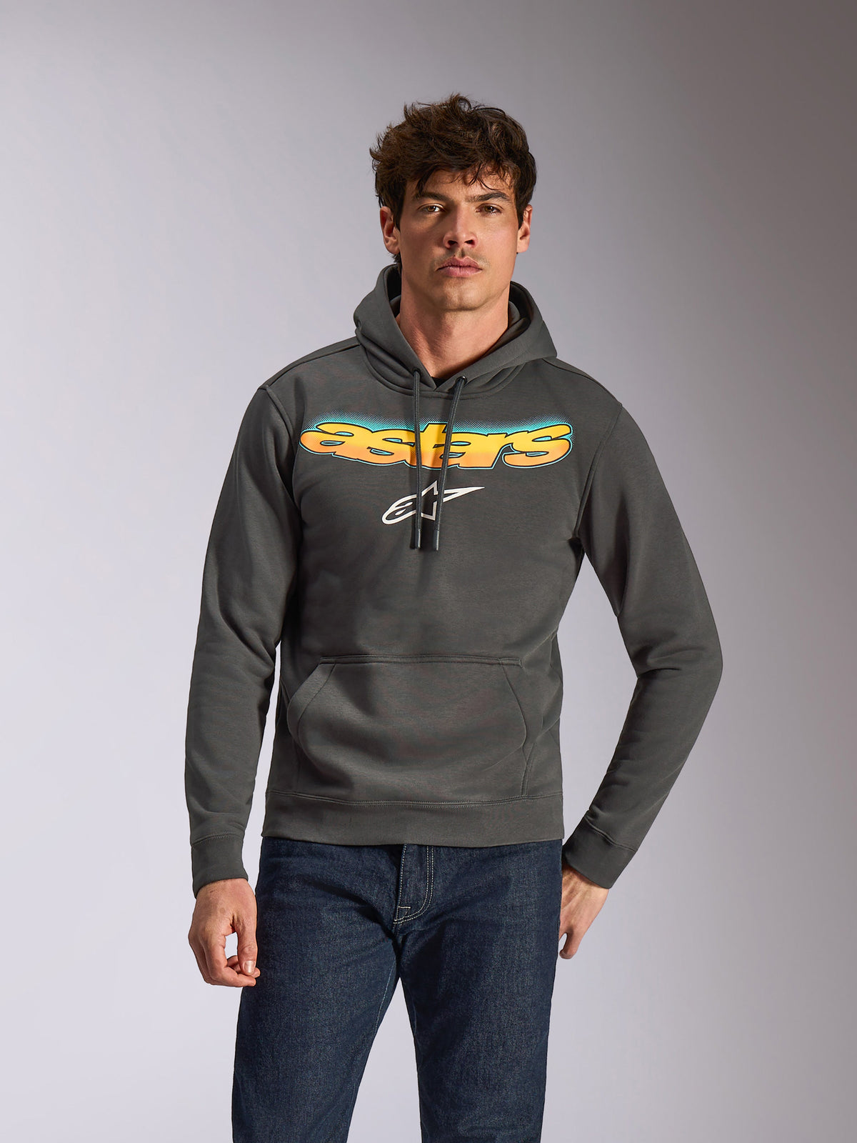 Alpinestars Ellipsoid hættetrøje, afslappet sportstøj, Gunmetal grå med gul og blå farveovergang på Astars-tekst og hvidt logo, pullover-design med hætte og snøre, båret med mørkeblå jeans