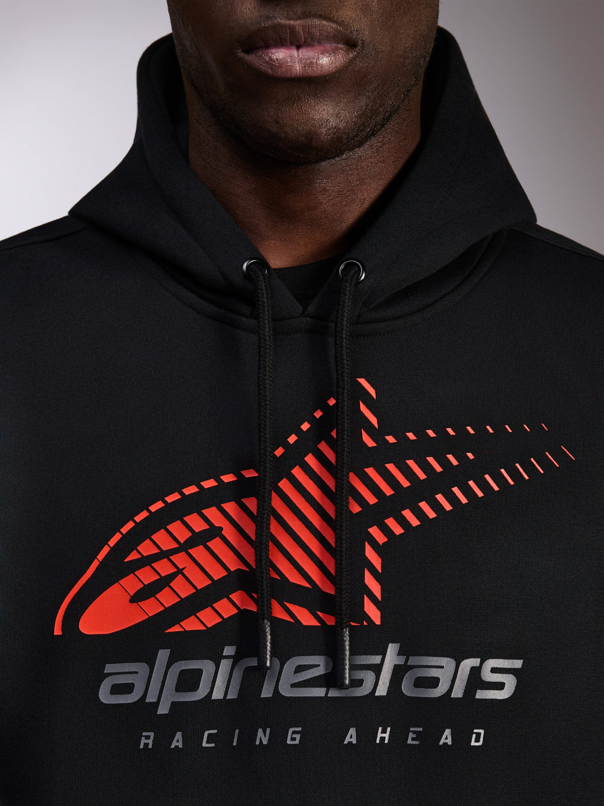 Alpinestars Pulse hættetrøje, sort pullover-hættetrøje, nærbillede af brystet med rødt Astars-logo med speed line-fade og sølvfarvet branding, sorte snore med dyppede ender, afslappet motorsport streetwear