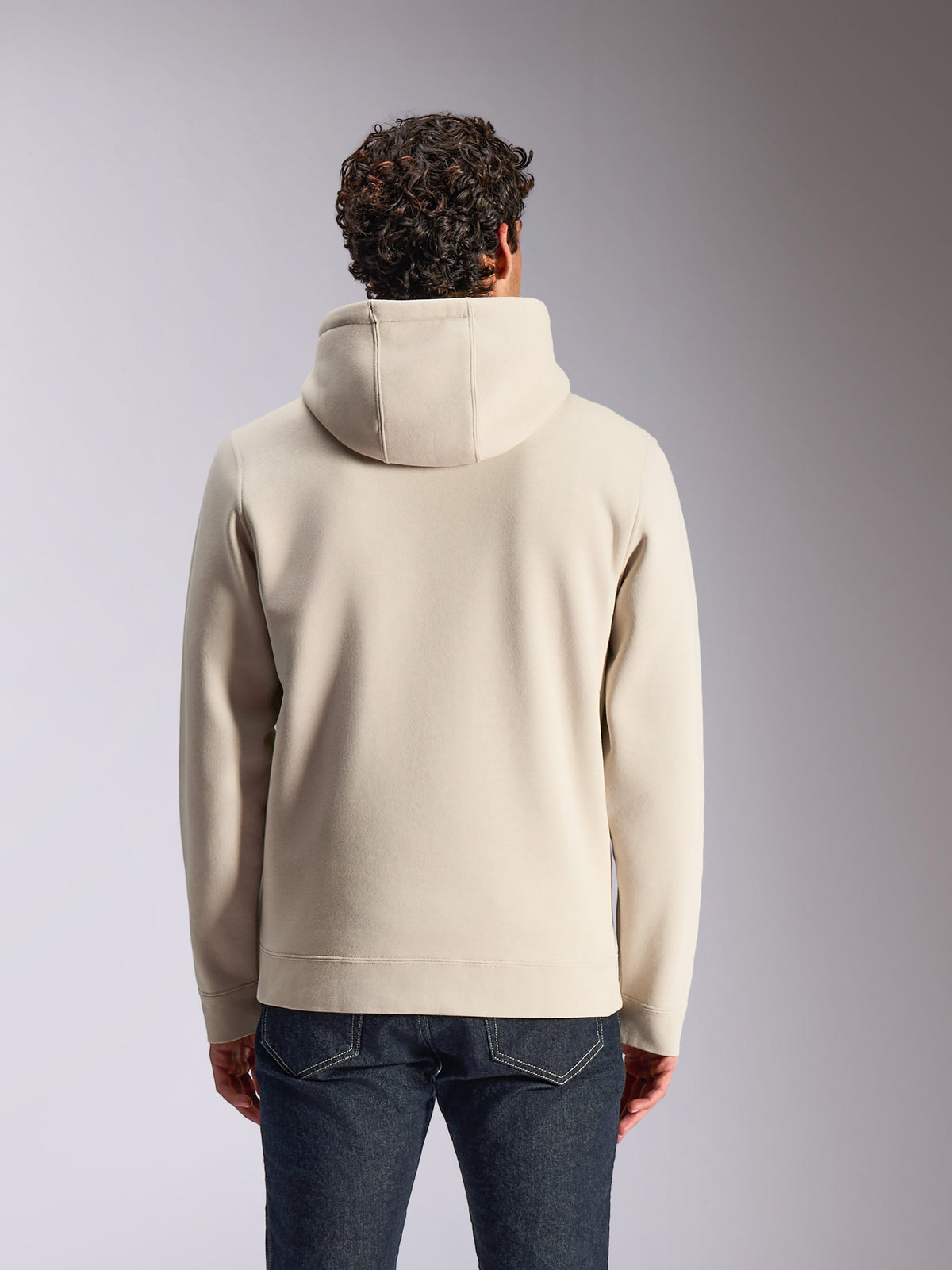 Alpinestars Pulse Hoodie, sandfarvet, bagfra af mandlig model iført den ensfarvede hættetrøje, kombineret med mørke denimjeans, afslappet motorsport-inspireret streetwear