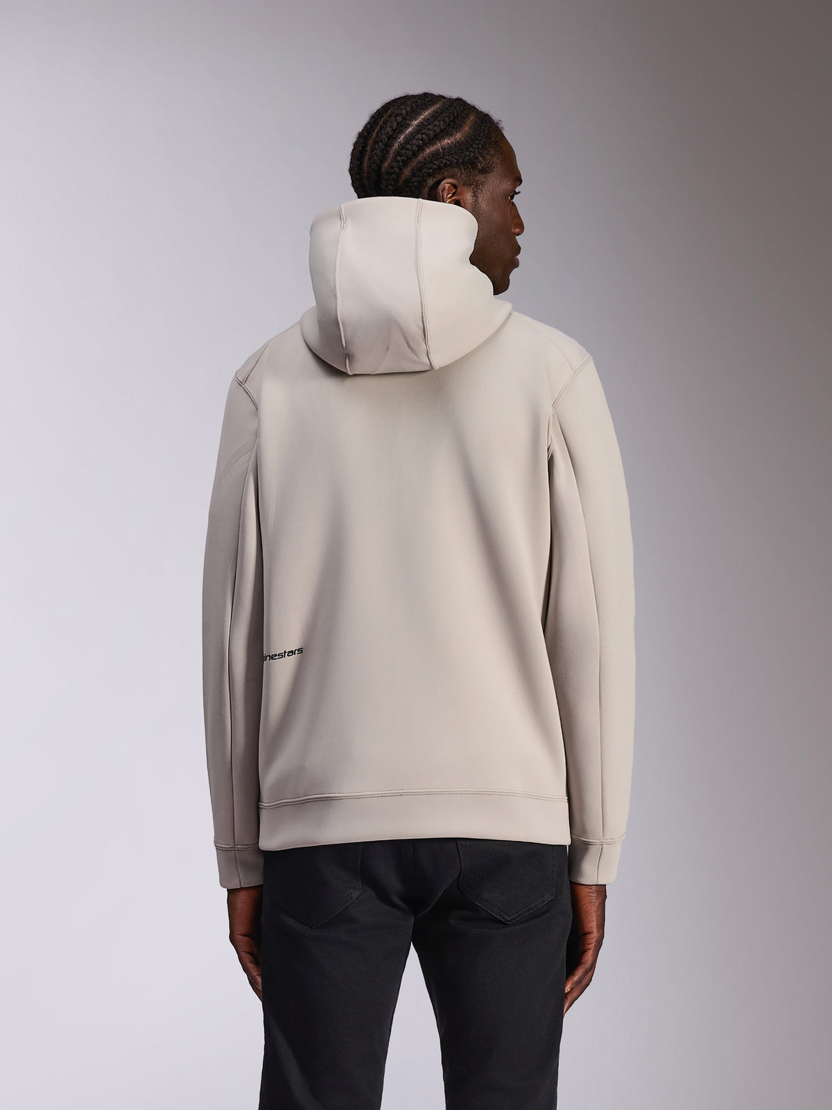 Alpinestars Cypher Hoodie, afslappet sportstøj, Cement-grå, set bagfra på model, hætte med høj hals, dobbeltsidet fleece-materiale, minimalt Alpinestars-logo nederst på ryggen, kombineret med sorte bukser