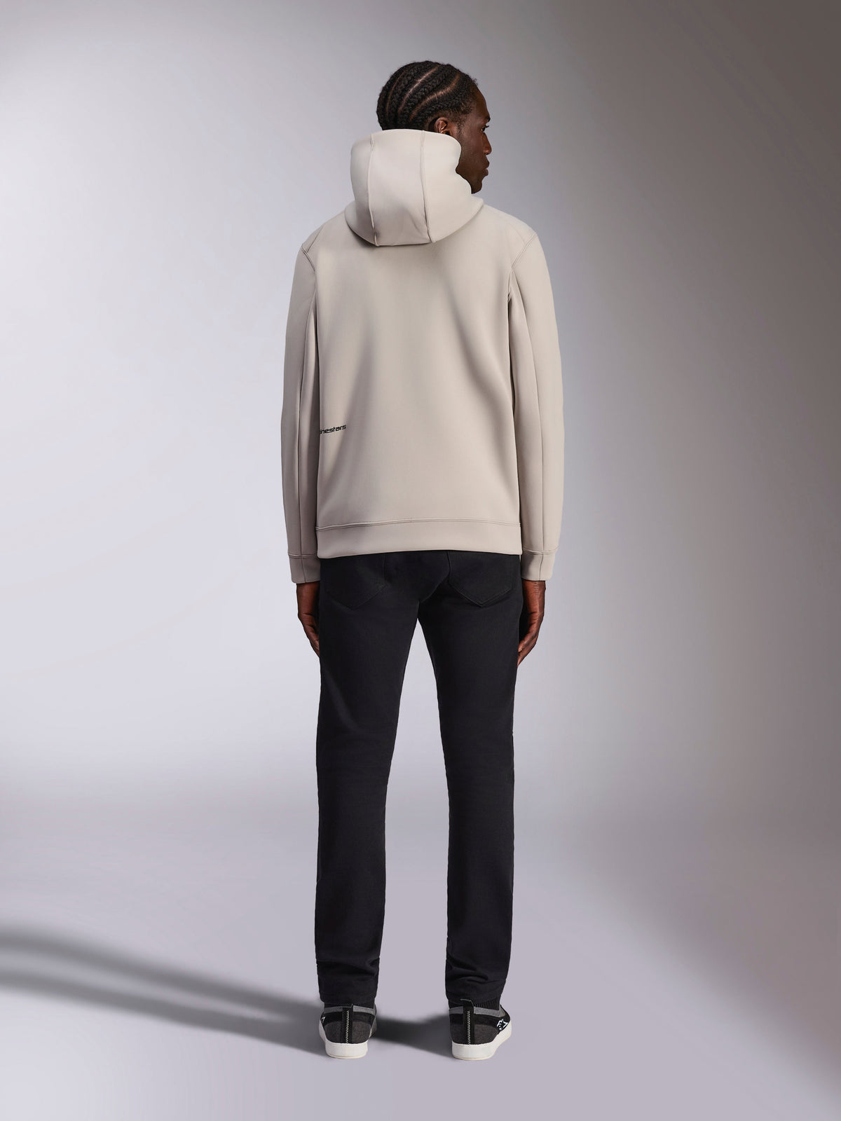Alpinestars Cypher hættetrøje, Cement lysegrå, set bagfra af mand iført fleecehættetrøje med gennemgående lynlås, høj hætte og Alpinestars-branding på ryggen, afslappet motorsport-inspireret streetwear kombineret med sorte bukser