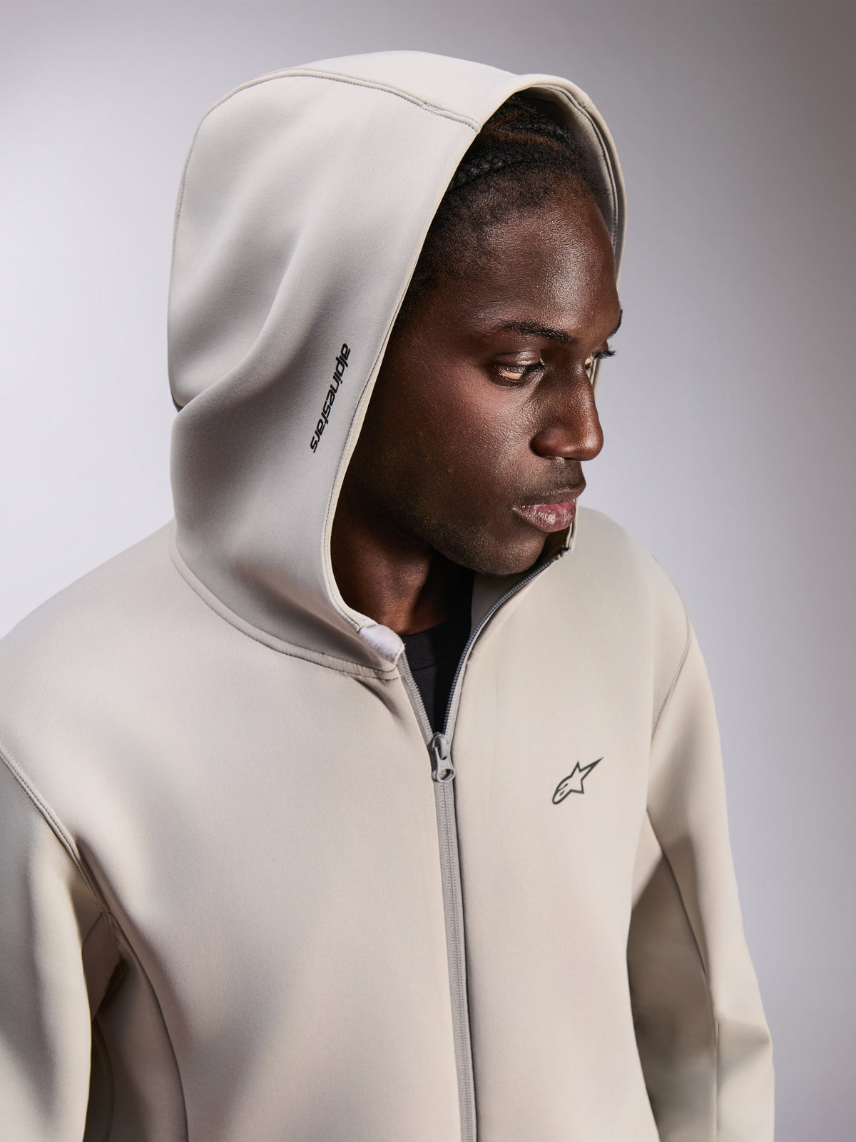 Alpinestars Cypher Hoodie, fleece-hættetrøje med lynlås, cementgrå, bæres med hætten oppe, med Alpinestars-ordlogo på hætten og lille Astars-logo på brystet, afslappet motorsport-inspireret streetwear