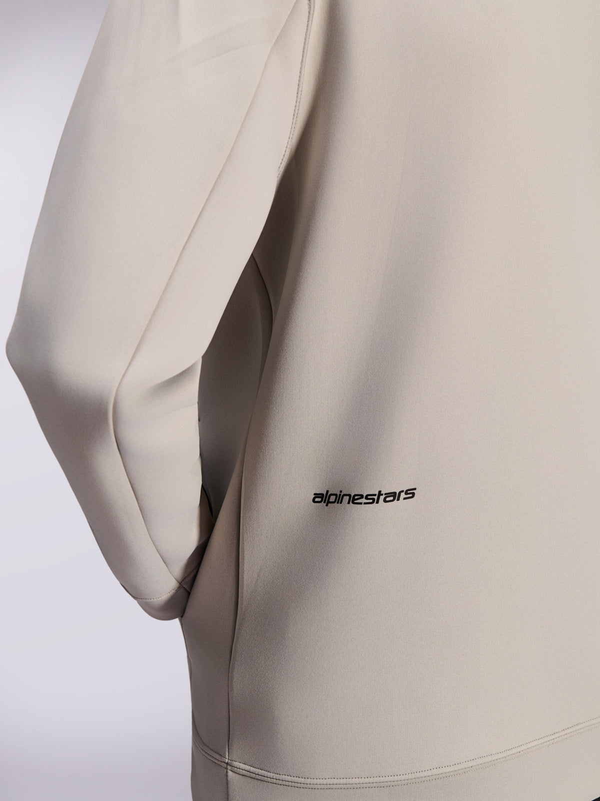 Alpinestars Cypher Hoodie, hættetrøje med lynlås i dobbeltsidet fleece, Cementgrå, nærbillede af lille sort Alpinestars-ordlogo nederst på ryggen, detalje af lomme i sømmen og glat tekstur i stoffet