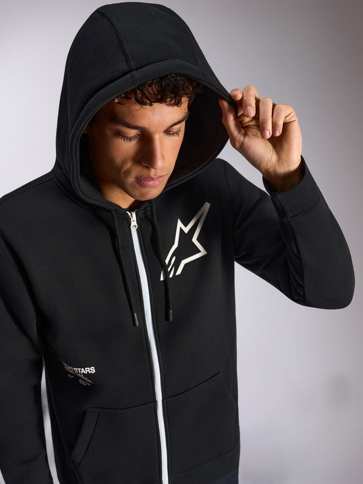 Alpinestars Transverse hættetrøje, sort hættetrøje med lynlås foran, hvidt Astars-logo på brystet, hvid lynlås, hætte med snoretræk trukket op, afslappet motorsport-inspireret streetwear