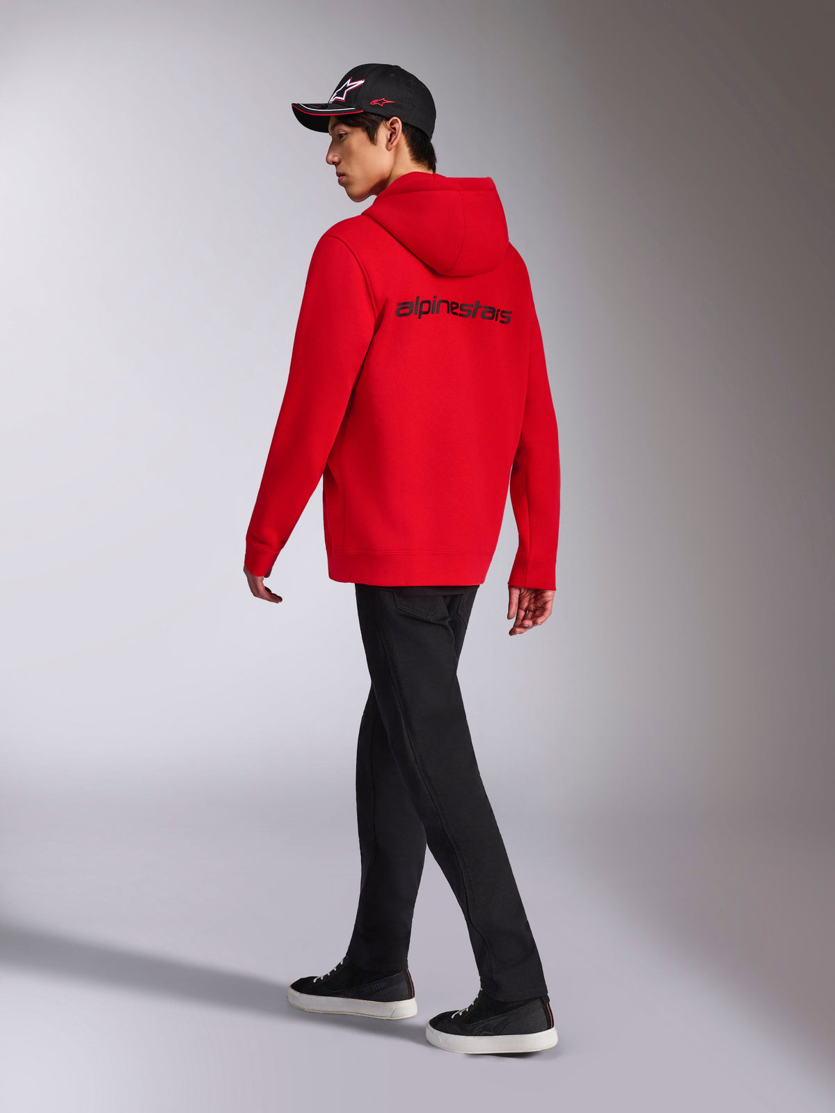 Alpinestars Transverse Hoodie, Red zip-up fleece hoodie, back view featuring black Alpinestars word logo, worn by a model with black pants and a black logo cap, casual motorsport-inspired streetwear