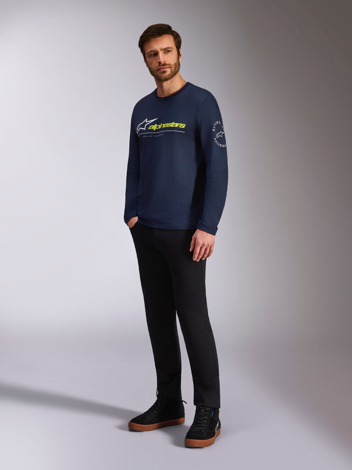 Alpinestars Mandatory CSF Tee, langærmet t-shirt, marineblå, med hvidt Astars-logo og gul Alpinestars-branding på fronten, Astars-cirkellogo på ærmet, båret af en model med sorte bukser og sorte sneakers for et afslappet lifestyle-look