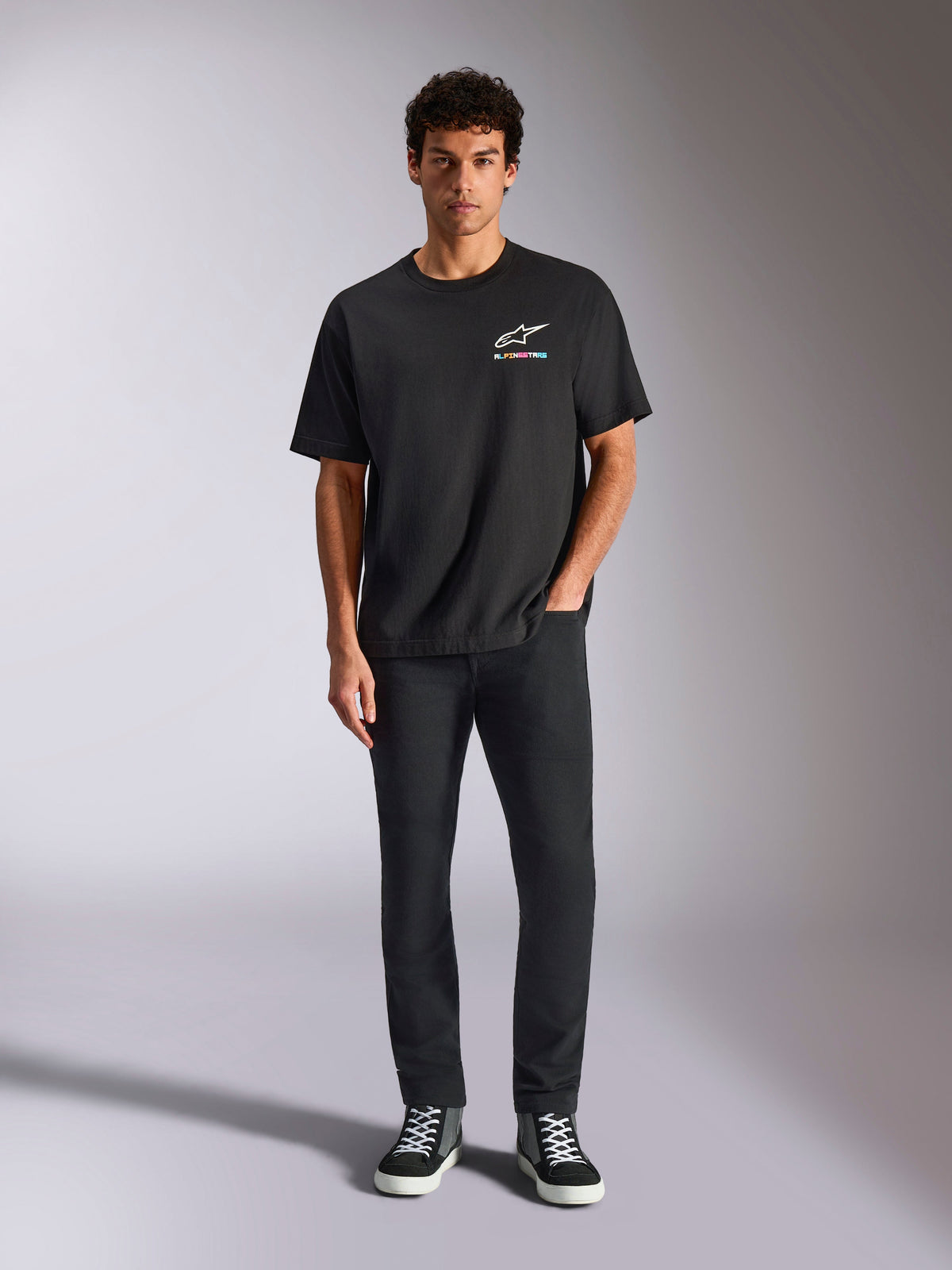 Alpinestars Wild Oversized CSF T-shirt, kortærmet T-shirt, sort, båret af en model med sorte bukser og sneakers, med et hvidt Astars-logo og livligt flerfarvet branding, afslappet motorsport streetwear