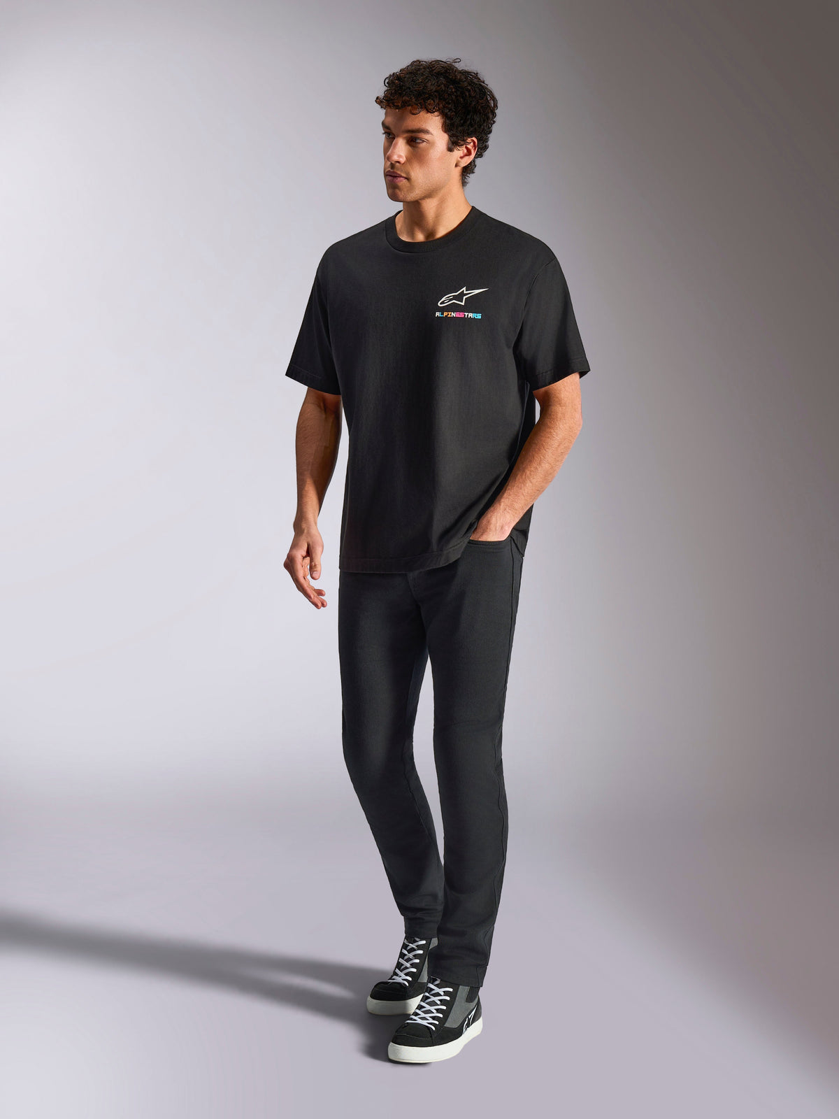 Alpinestars Wild Oversized CSF Tee, kortærmet T-shirt, sort, flerfarvet Astars-logo på brystet, afslappet streetwear-stil båret af en model med sorte bukser og high-top sneakers