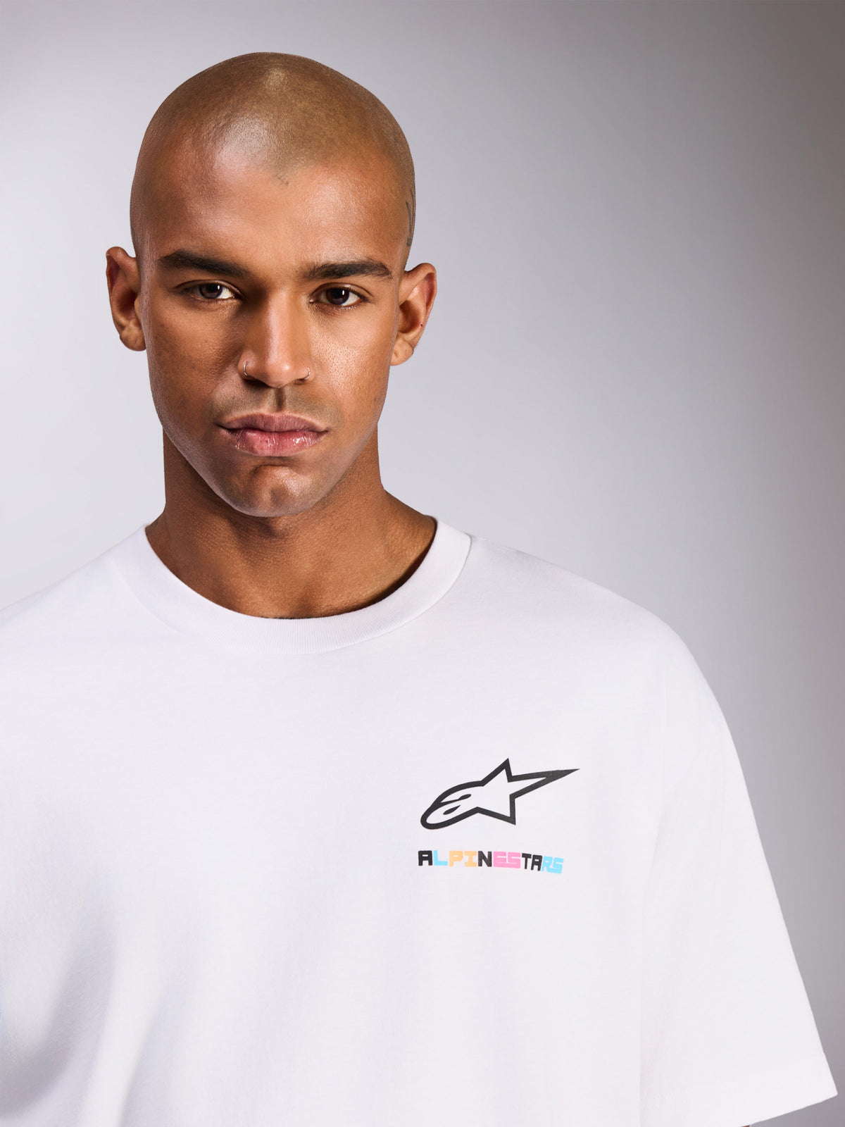 Male model wearing Alpinestars Wild Oversized CSF Tee, Short Sleeve T-Shirt, White, featuring black Astars logo with vibrant multicolor lettering on the chest, casual streetwear style