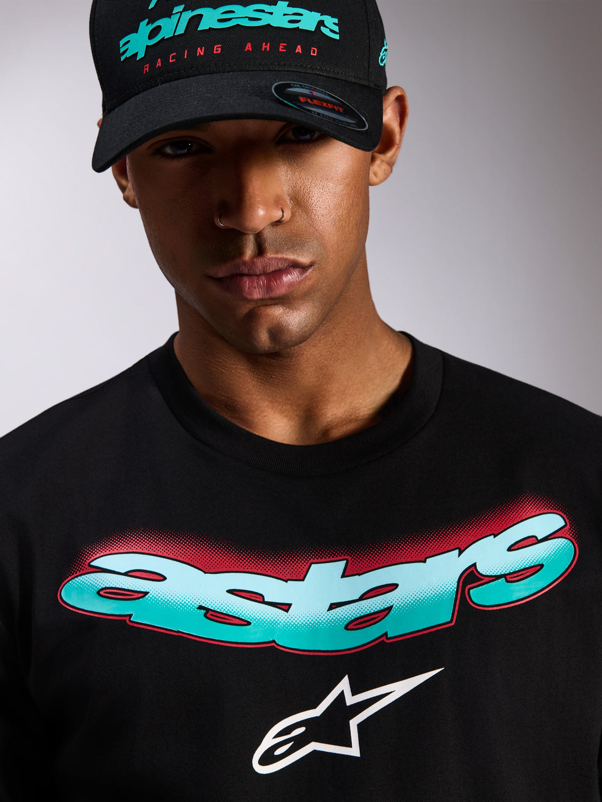 Alpinestars Ellipsoid CSF T-shirt, kortærmet T-shirt, sort, Astars-tekstlogo med blågrøn og hvid farveovergang og røde halvtone-detaljer, hvidt Astars-logo, bæres med matchende sort Alpinestars-kasket, afslappet motorsport-streetwear