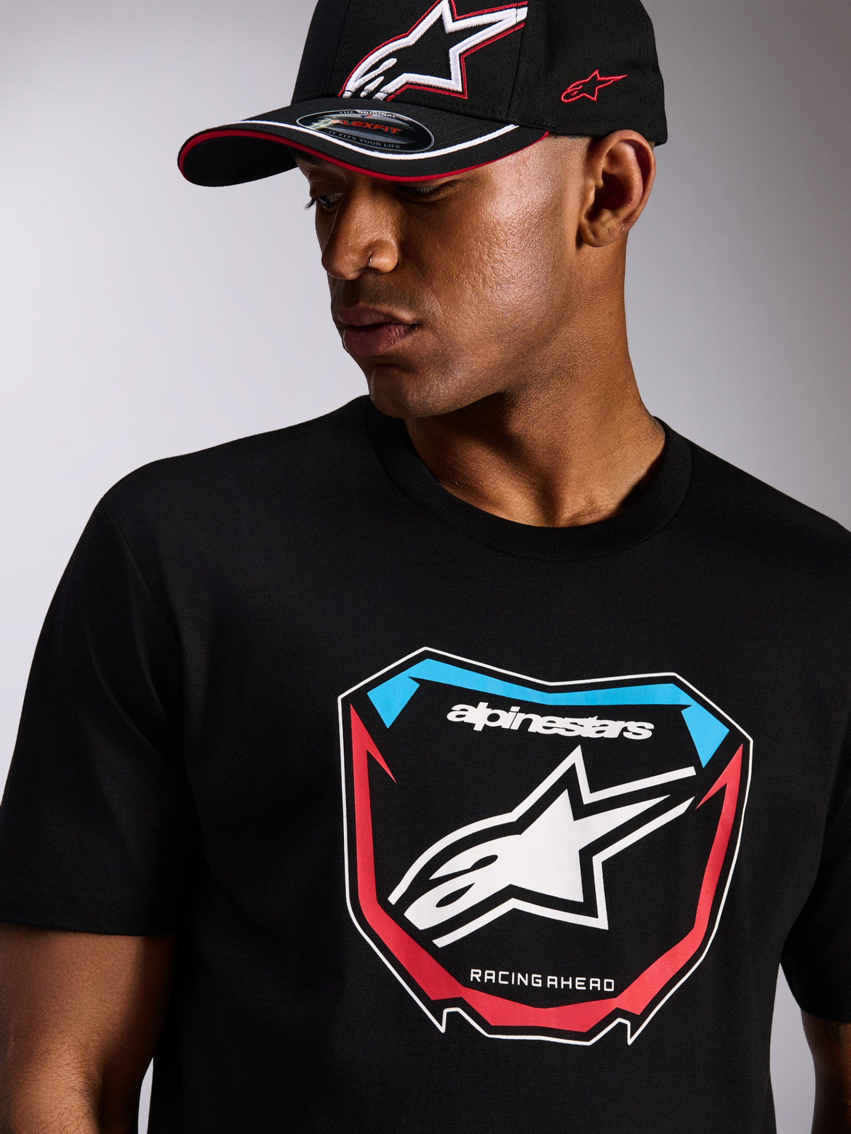 Alpinestars Plate CSF Tee, kortærmet t-shirt, sort, stor MX-plade grafik på forsiden med stjernelogo og røde og blå detaljer, båret med en matchende sort Alpinestars kasket, afslappet motorsport streetwear