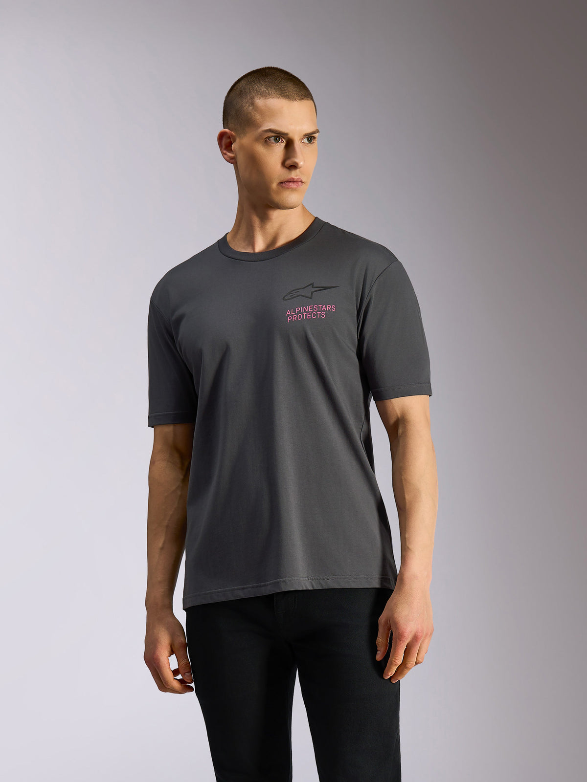Alpinestars Pop Helmet CSF Tee, kortærmet t-shirt, koksgrå, båret af model, med sort Astars-logo og lyserød 'ALPINESTARS PROTECTS' tekst på brystet, afslappet motorsport-streetwear