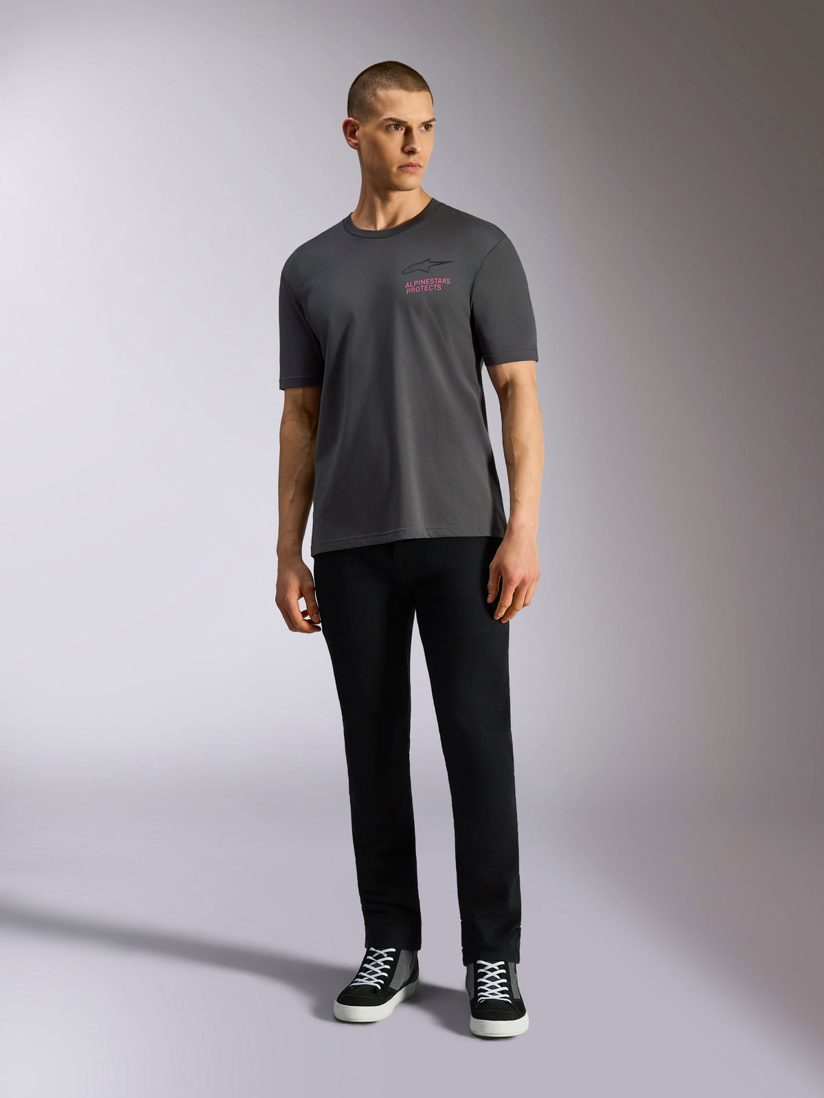 Alpinestars Pop Helmet CSF Tee, kortærmet T-shirt, koksgrå, med et lyserødt Alpinestars-logo på brystet, båret af en mandlig model med sorte bukser og sneakers, afslappet motorsport-streetwear