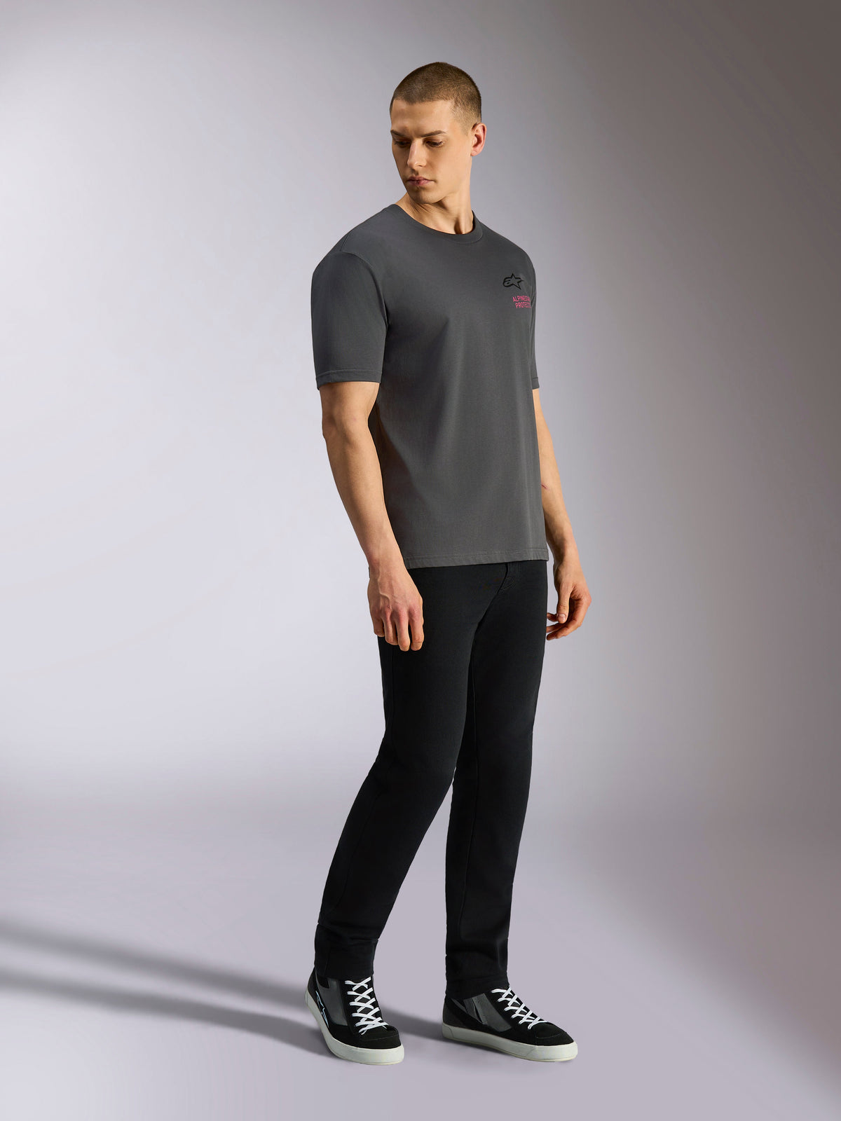 Alpinestars Pop Helmet CSF Tee, kortærmet T-shirt, koksgrå, bæres af model med sorte bukser og sneakers, med sort Astars-logo og lyserød tekst på forsiden, afslappet motorsport-streetwear