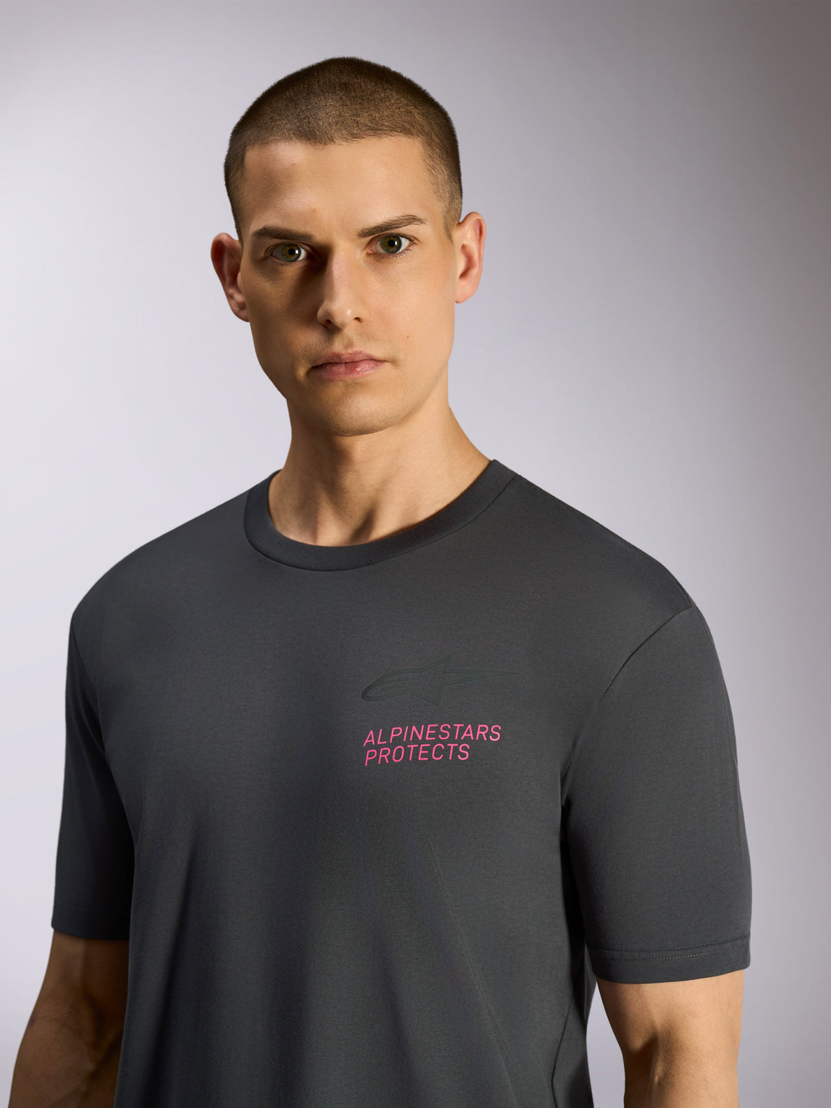Alpinestars Pop Helmet CSF Tee, kortærmet T-shirt, koksgrå, båret af model, med lyserød 'ALPINESTARS PROTECTS' tekst og Astars-logo på brystet, afslappet motorsport streetwear