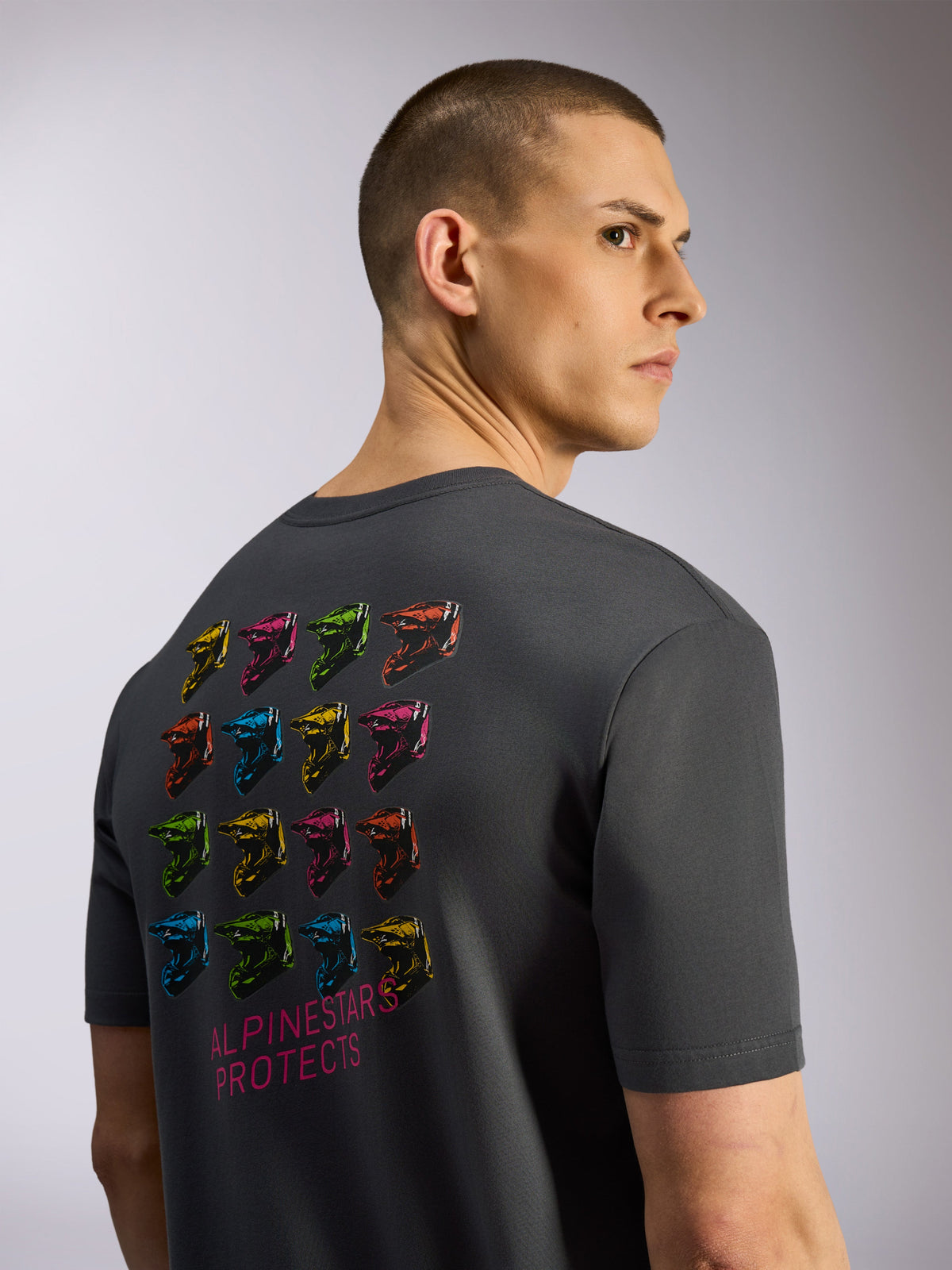 Alpinestars Pop Helmet CSF Tee, kortærmet t-shirt, koksgrå, set bagfra med et gitter af farverige M10-hjelme og 'Alpinestars Protects'-tekst, afslappet motorsport-streetwear