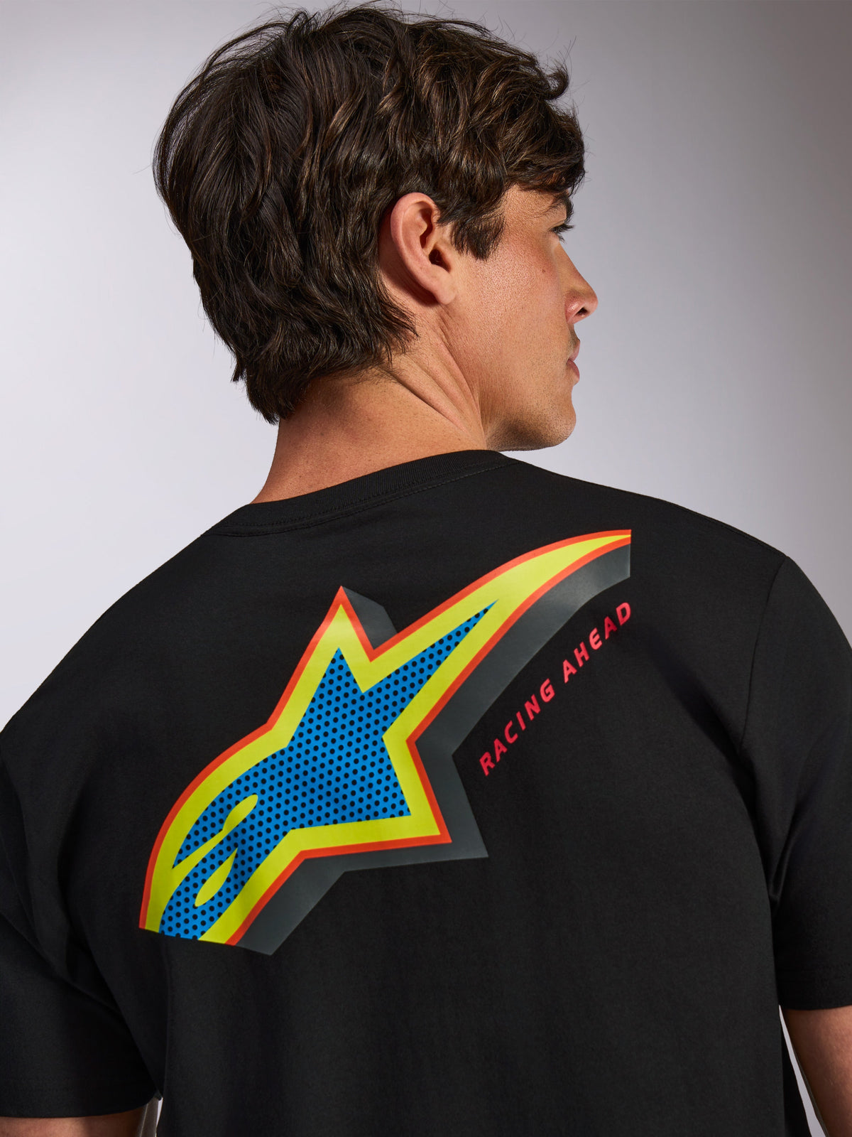 Alpinestars Angler CSF Tee, kortærmet T-shirt, sort, stort flerfarvet Astars-logo på ryggen med blåt perforeret fyld, gule og røde konturer og 'RACING AHEAD'-tekst, afslappet motorsport-streetwear