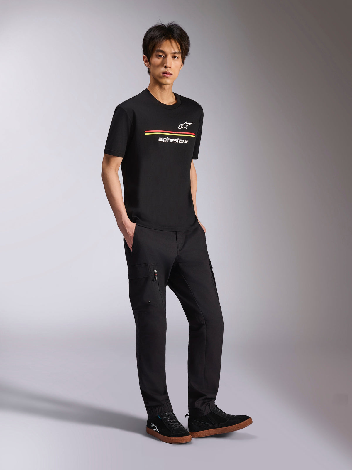 Alpinestars Lanes CSF Tee, Short Sleeve T-Shirt, Black, Multicolor Astars and Alpinestars stripe logos on chest, worn by model with black cargo pants, casual motorsport streetwear