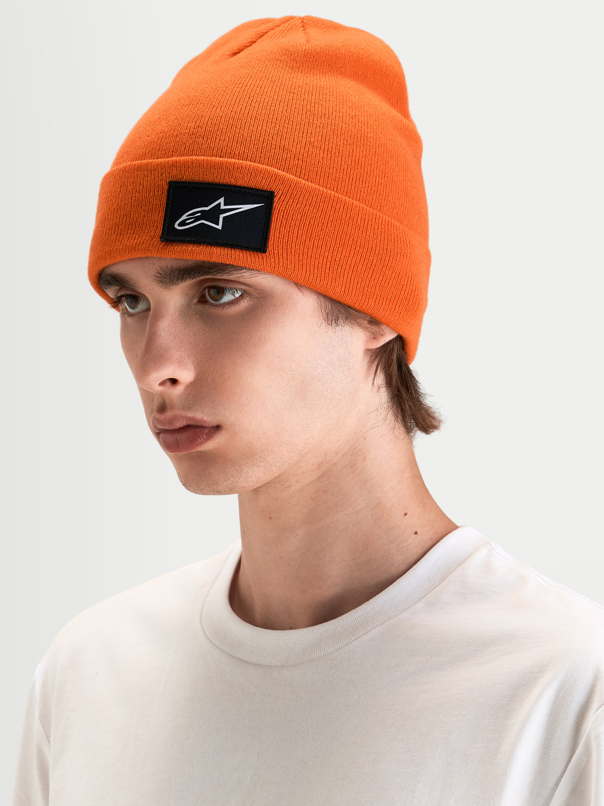 Alpinestars Augment Cuff Beanie, orange strikket beanie med sort og hvidt vævet Astars-logo, båret af mandlig model i afslappet tøj