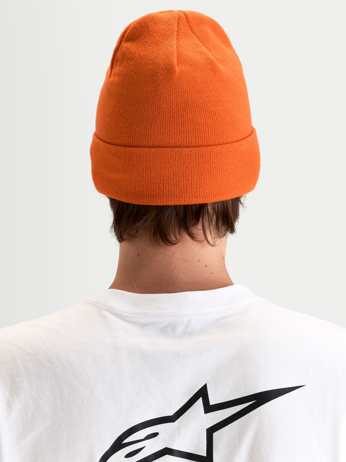Alpinestars Augment Cuff Beanie, orange strikket hue med opslag, set bagfra på en model iført en hvid t-shirt med sort Astar-logo